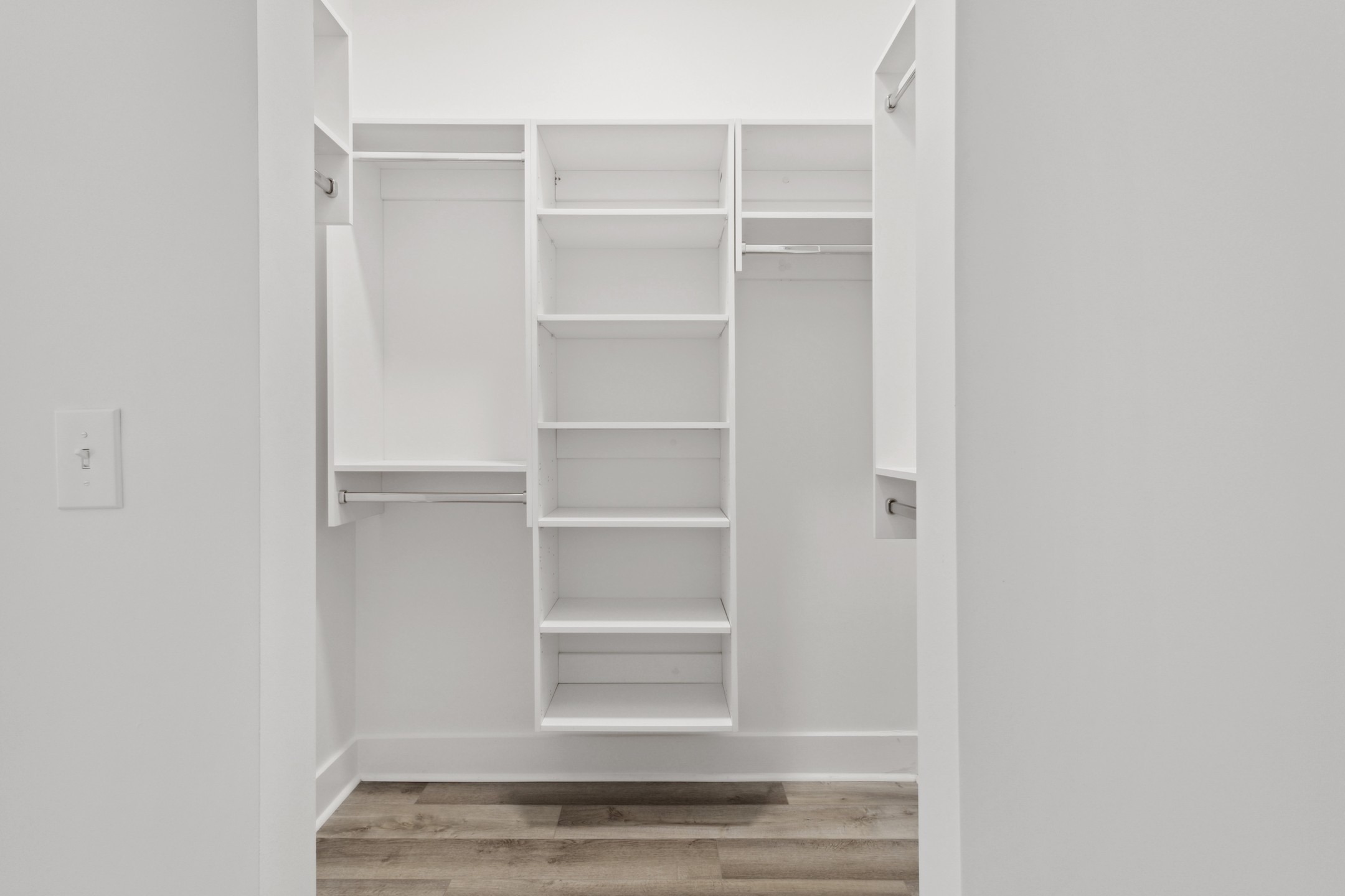 Interior view of AMLI Old 4th Ward  walk in closet with built in white wood shelving and silver hanging poles with white walls 