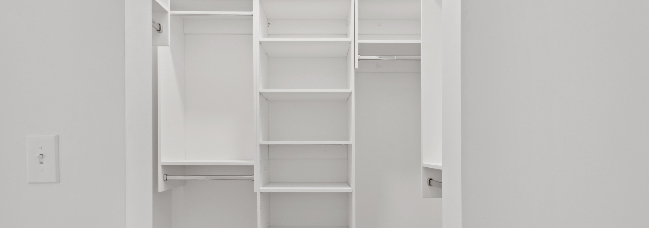 Interior view of AMLI Old 4th Ward  walk in closet with built in white wood shelving and silver hanging poles with white walls