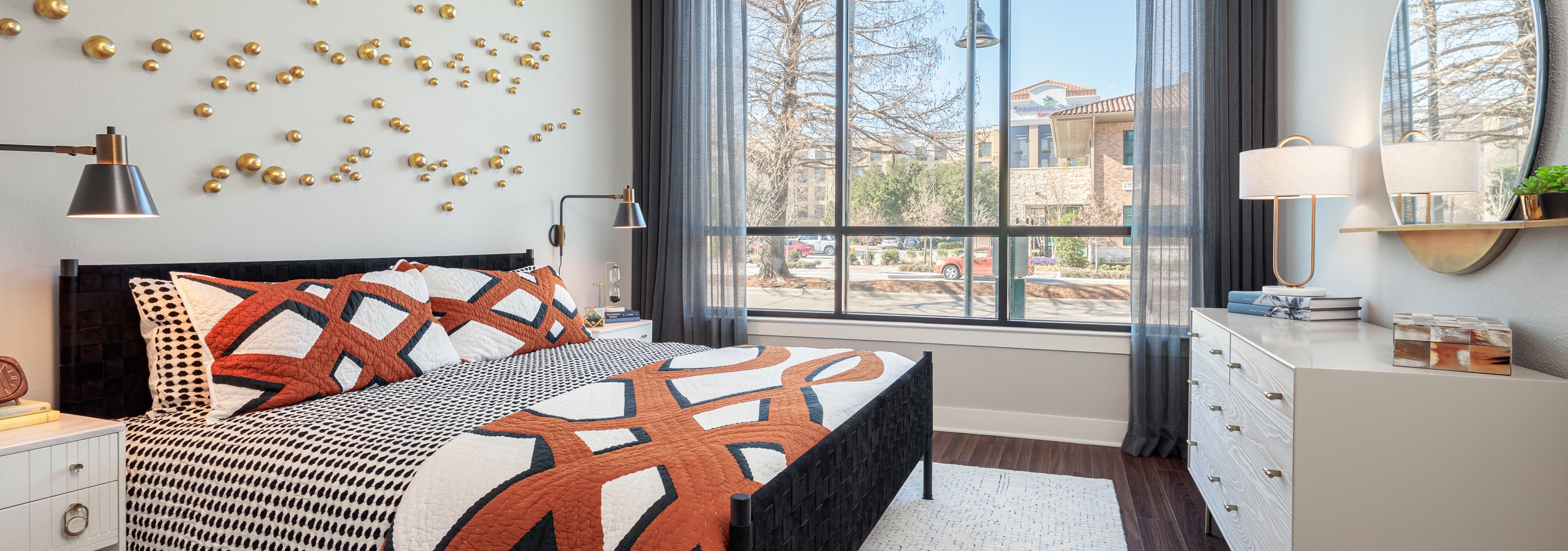 AMLI Addison bedroom with large windows and sheer black curtains with dark hardwood and patterned orange and white bedding