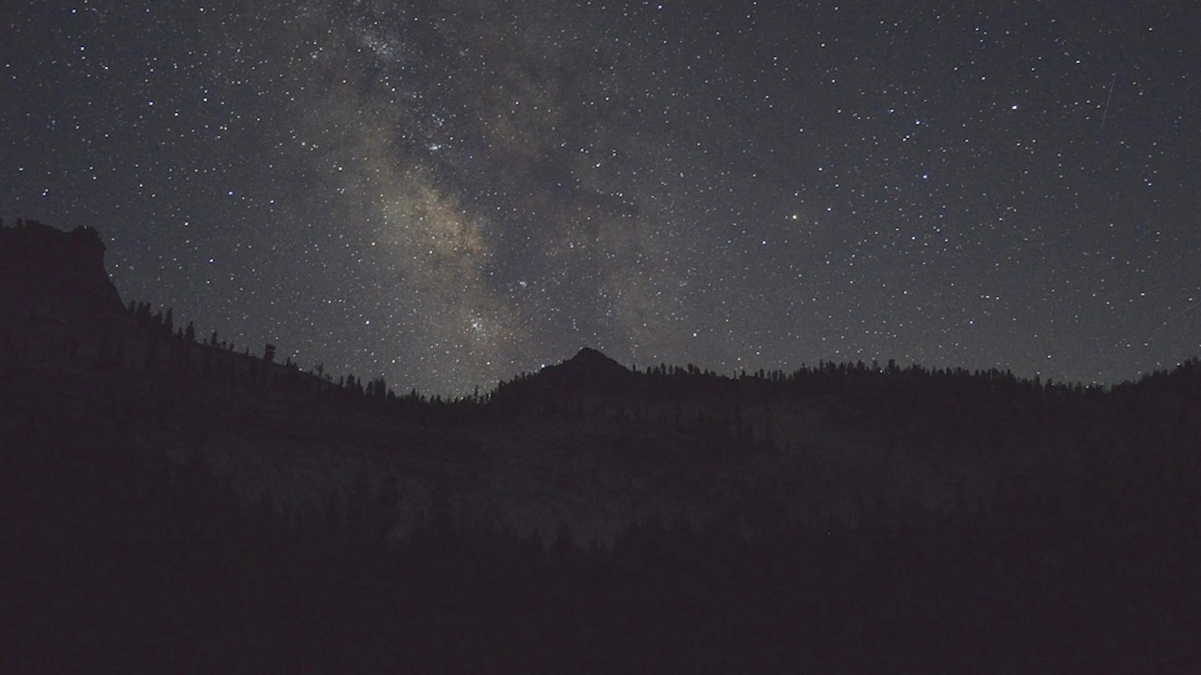 A clear night sky with the Milky Way shining brightly in the center set against a silhouette of mountains