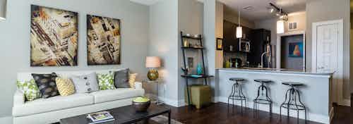 A living room and kitchen at AMLI Arista apartments with a view of couches and artwork and a granite kitchen counter top