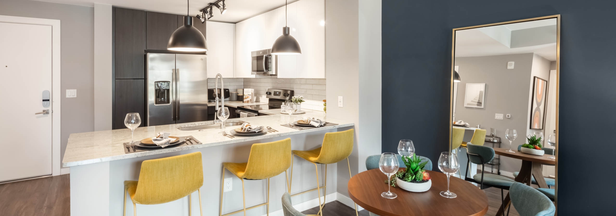 AMLI at Uptown modern apartment kitchen with blue chairs around a small wooden table and yellow barstools at granite counter