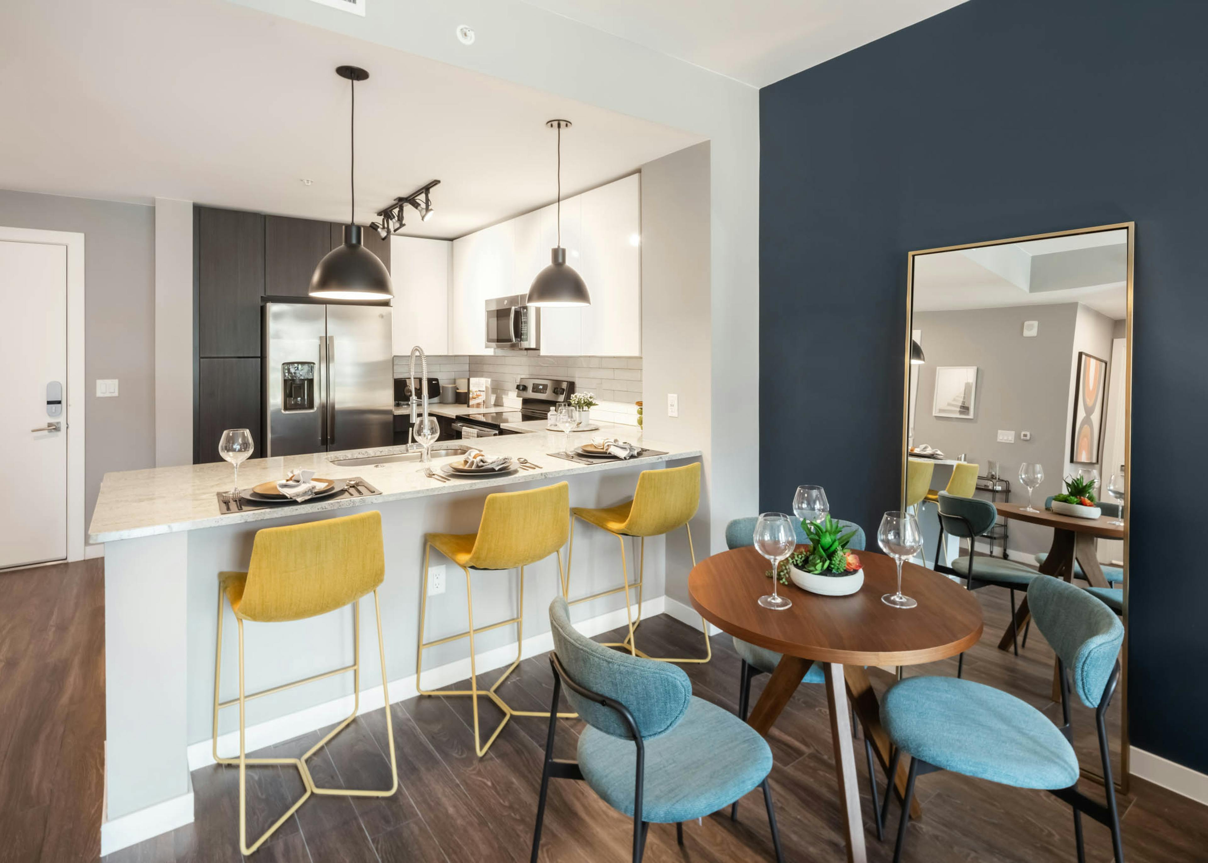 AMLI at Uptown modern apartment kitchen with blue chairs around a small wooden table and yellow barstools at granite counter
