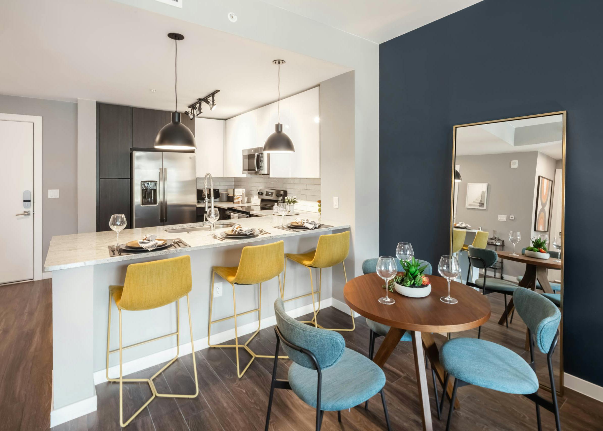 AMLI at Uptown modern apartment kitchen with blue chairs around a small wooden table and yellow barstools at granite counter