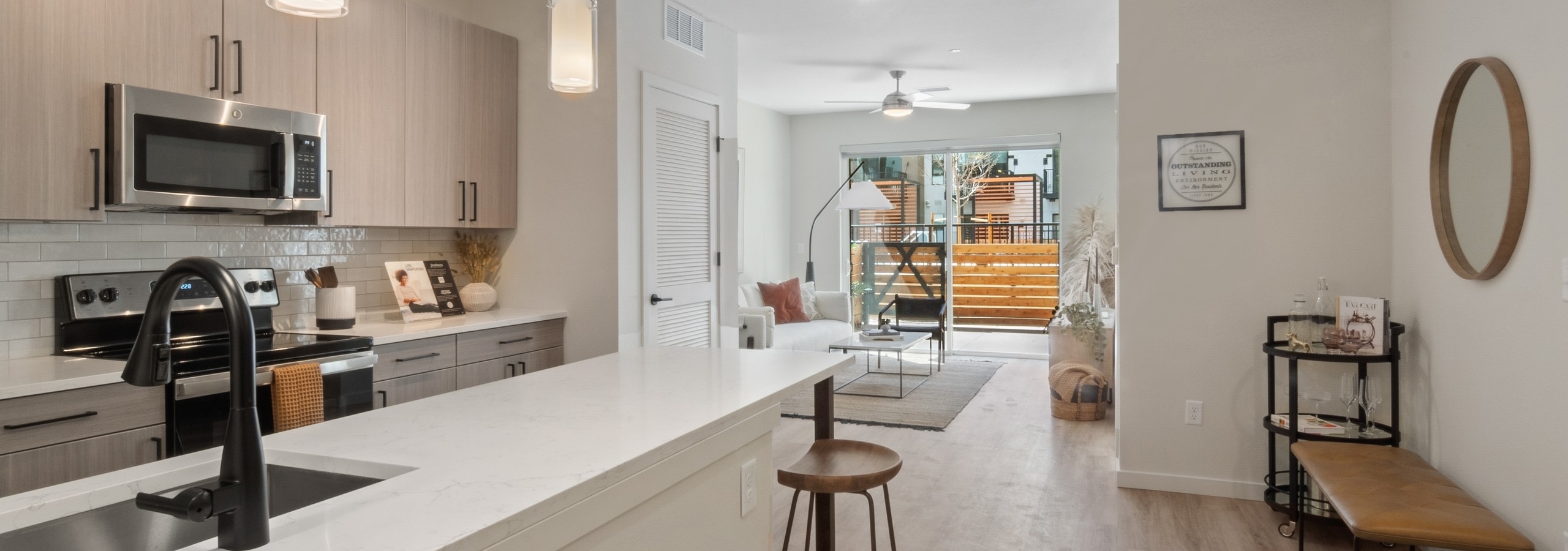 Apartment island kitchen at AMLI Broadway Park with white quartz countertop and bar seating with a view into the living room