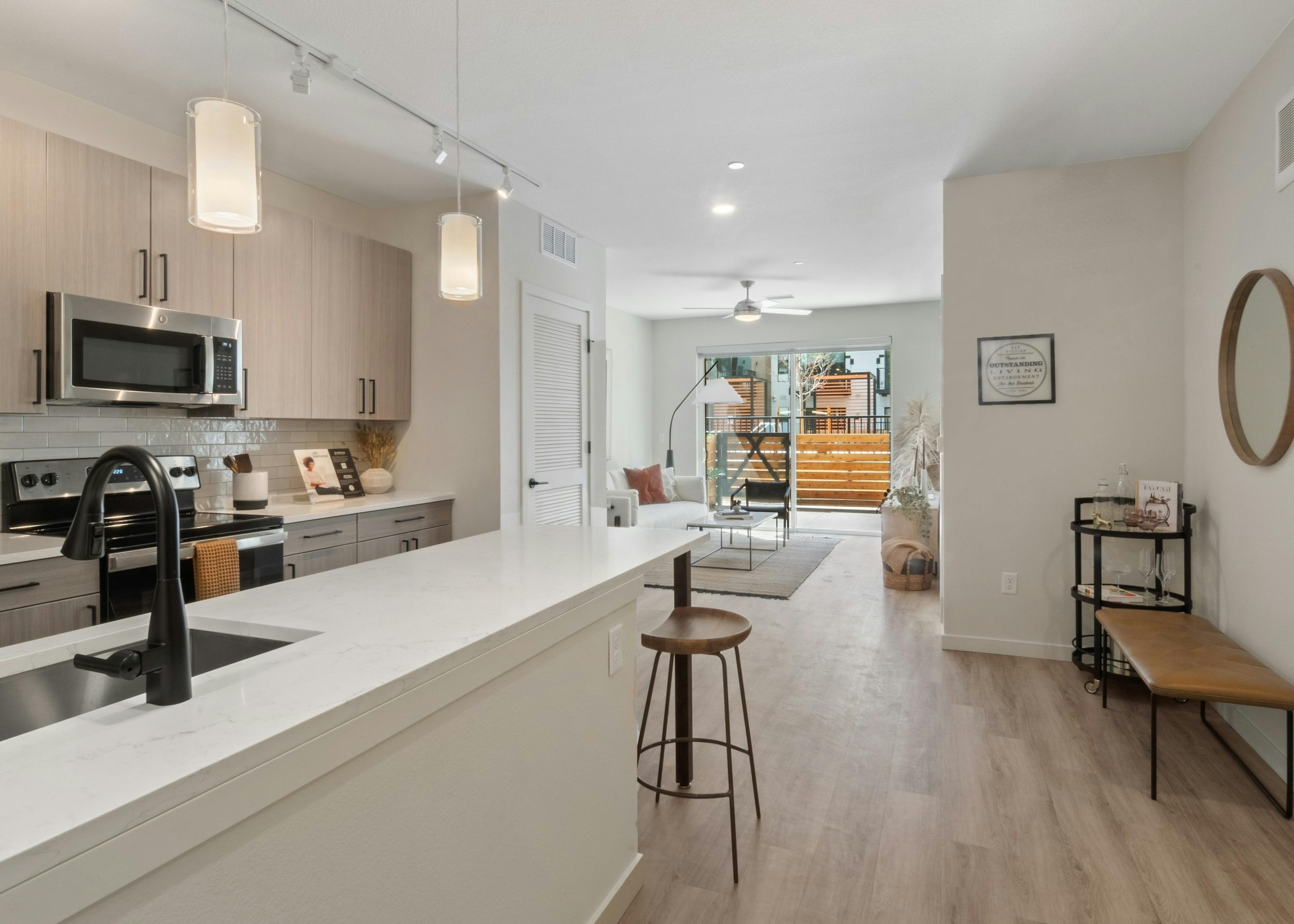 Apartment island kitchen at AMLI Broadway Park with white quartz countertop and bar seating with a view into the living room