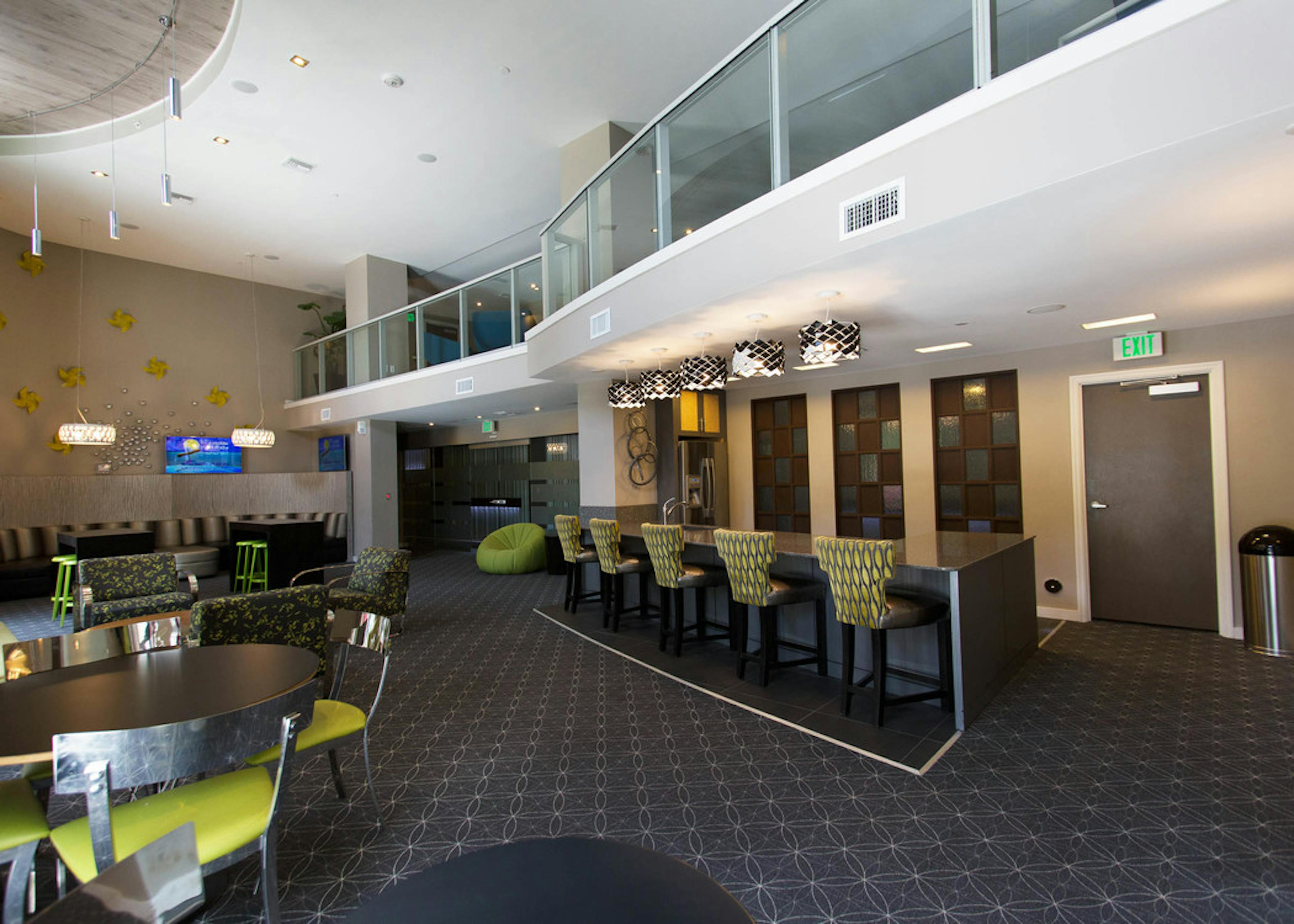 Two story resident lounge at AMLI Dadeland with bright green accent furniture and fully equipped kitchen with bar stools