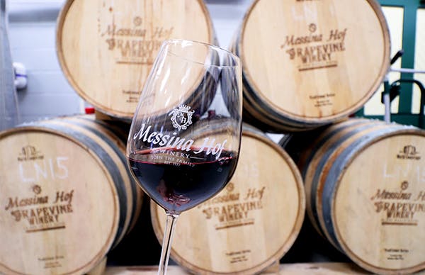 A wine glass half-full of red wine against a backdrop of wine barrels