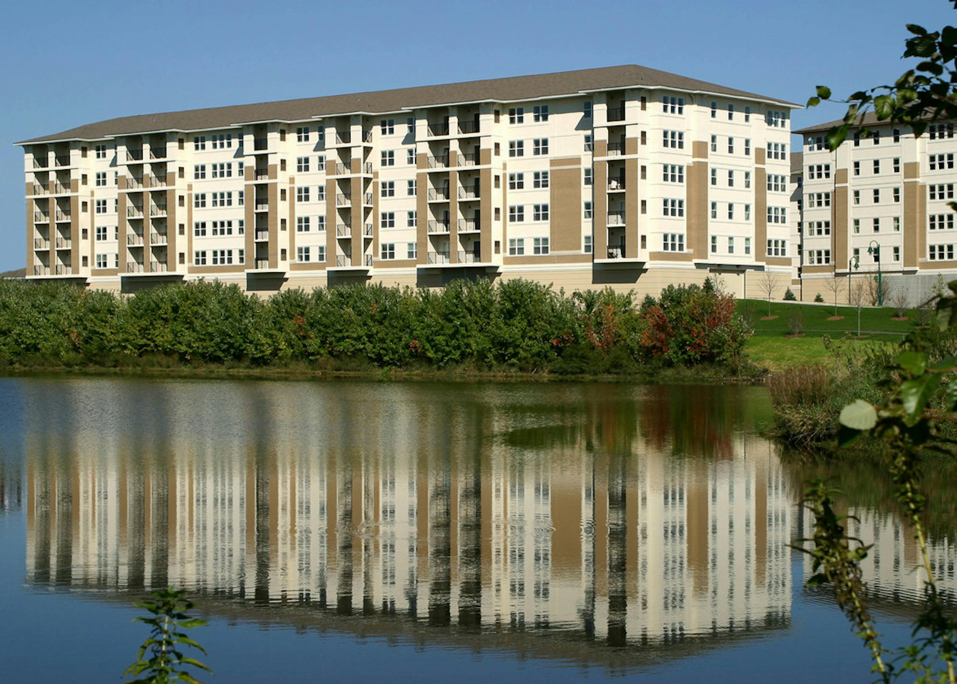 Exterior view of the lakeside AMLI at Seven Bridges apartment community building with a brown and ivory brick facade