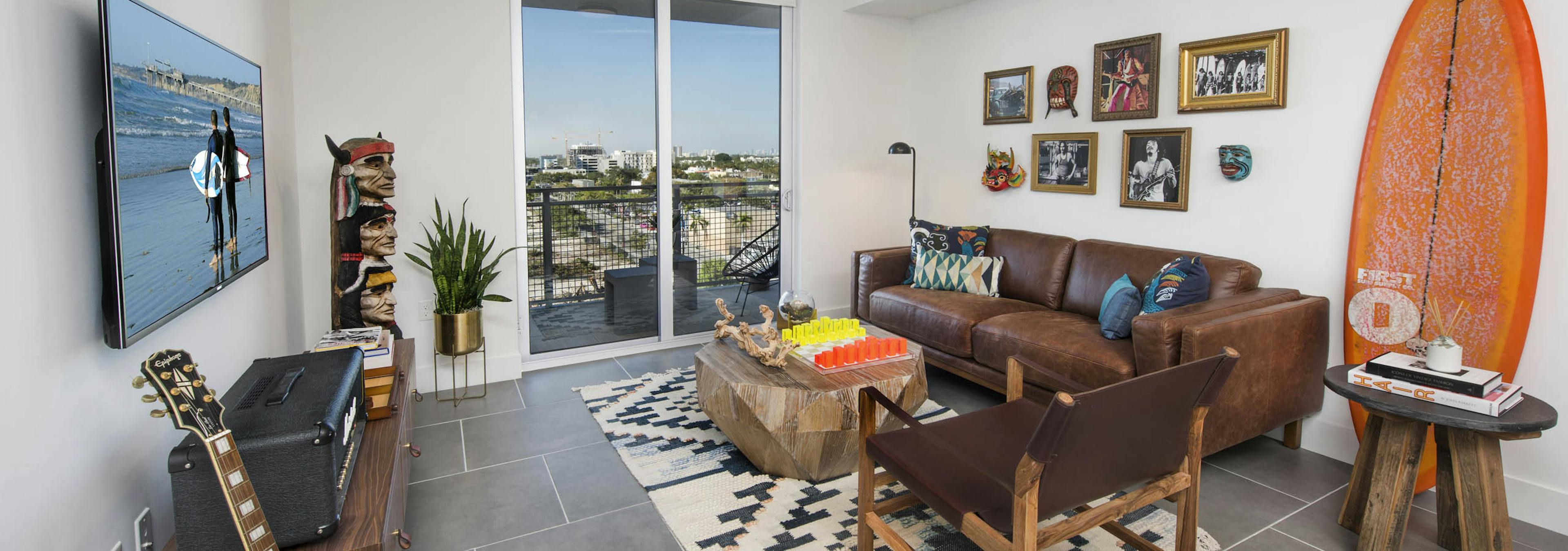 Living room with balcony view of city and orange surfboard on wall with leather couch and totem pole art at AMLI Midtown 29