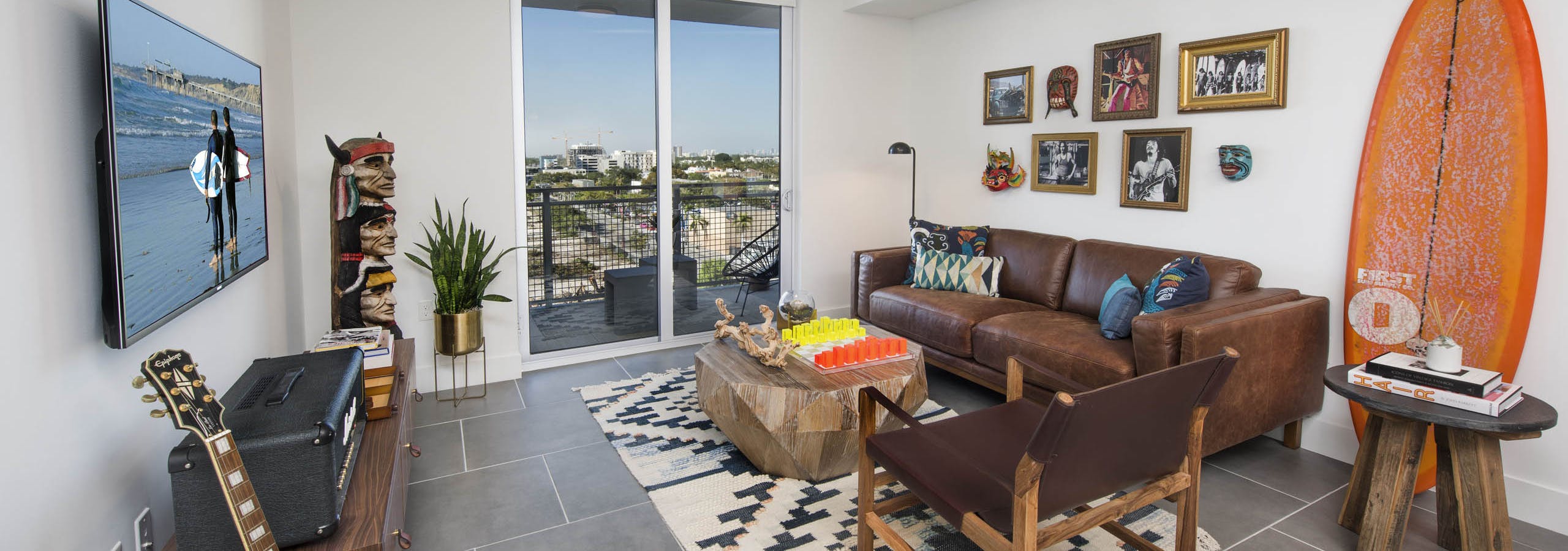 Living room with balcony view of city and orange surfboard on wall with leather couch and totem pole art at AMLI Midtown 29