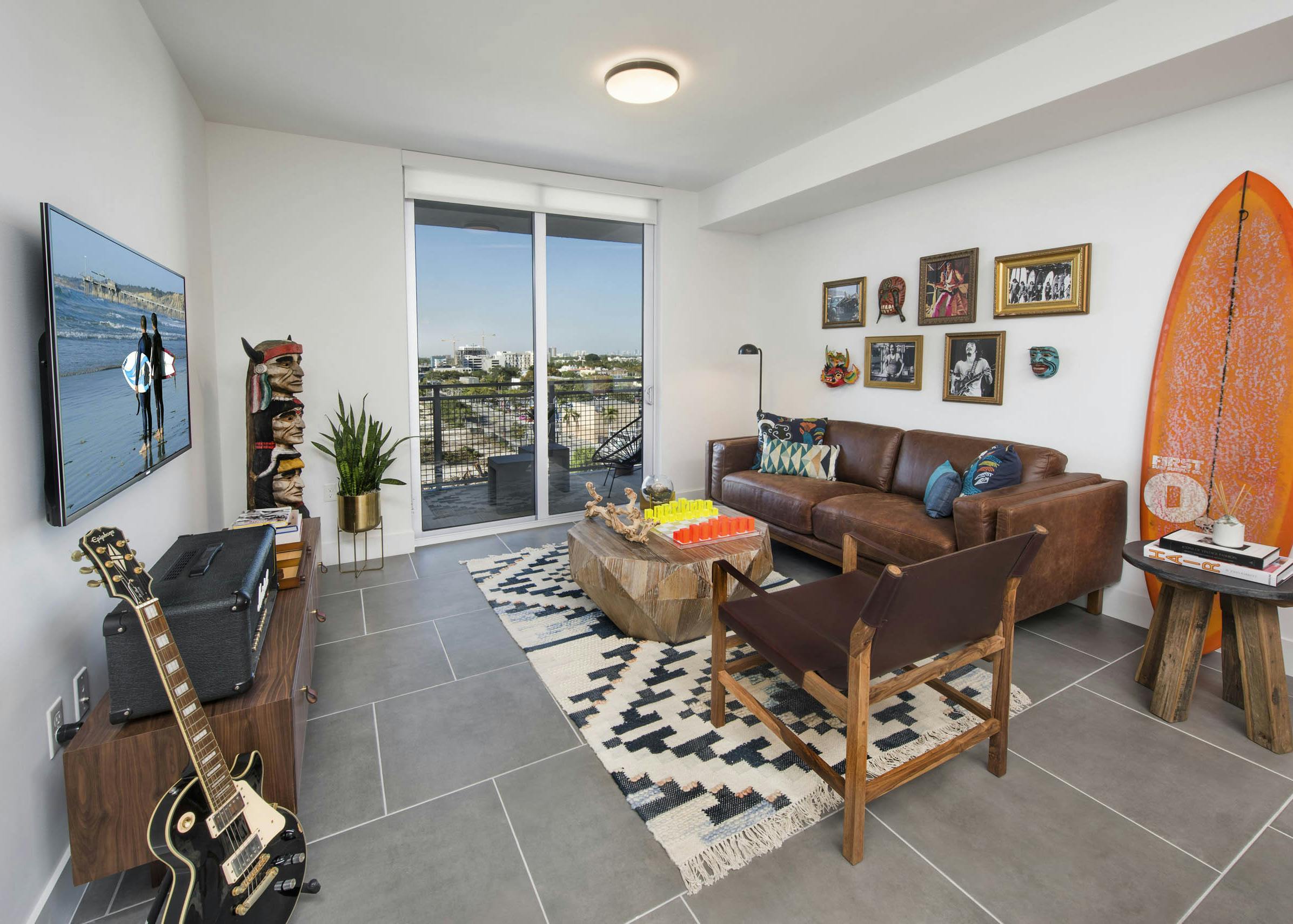 Living room with balcony view of city and orange surfboard on wall with leather couch and totem pole art at AMLI Midtown 29