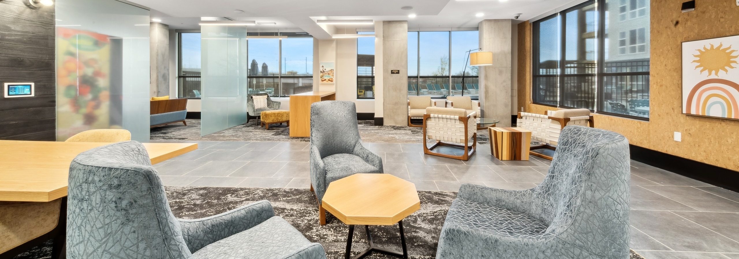 Business center at AMLI RiNo with 3 blue velvet chairs and other seating and tables with a view of pool and skyline