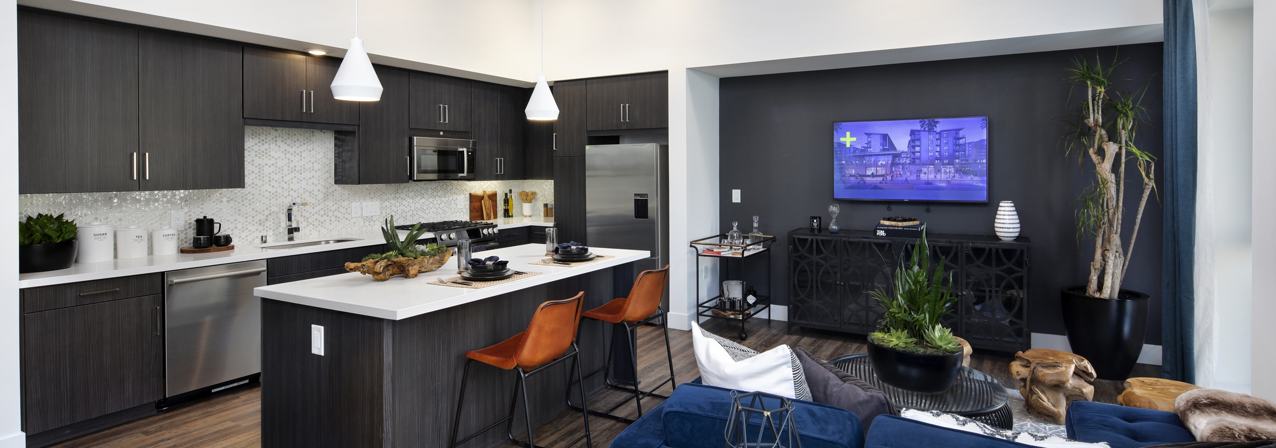 Interior of AMLI Marina Del Rey kitchen island with fully set quartz countertop, dark cabinets and blue sofa in living room