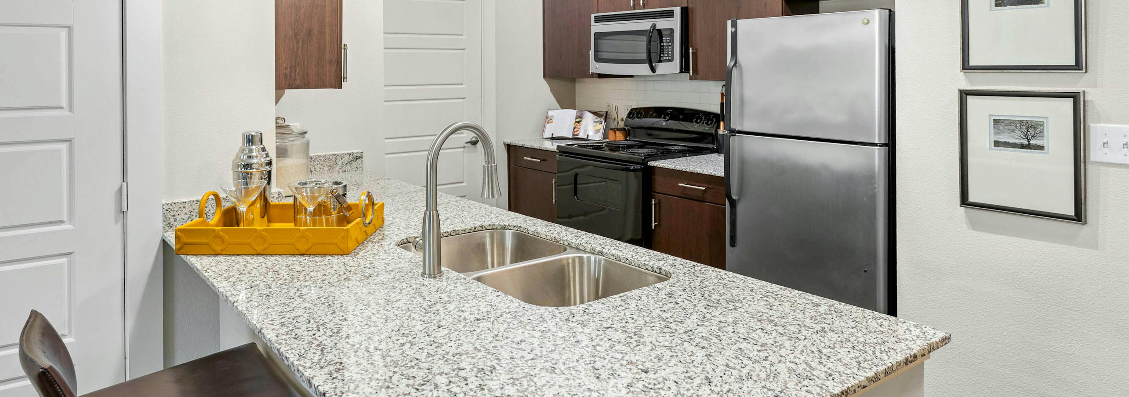AMLI at Escena apartment kitchen with wooden cabinets and a yellow tray with drinking glasses on granite countertop 