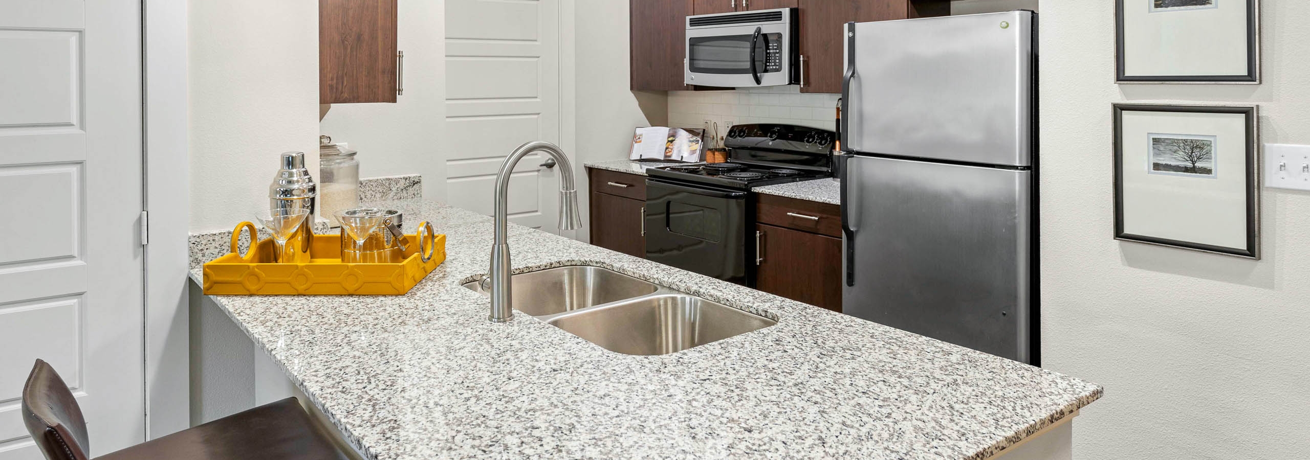 AMLI at Escena apartment kitchen with wooden cabinets and a yellow tray with drinking glasses on granite countertop