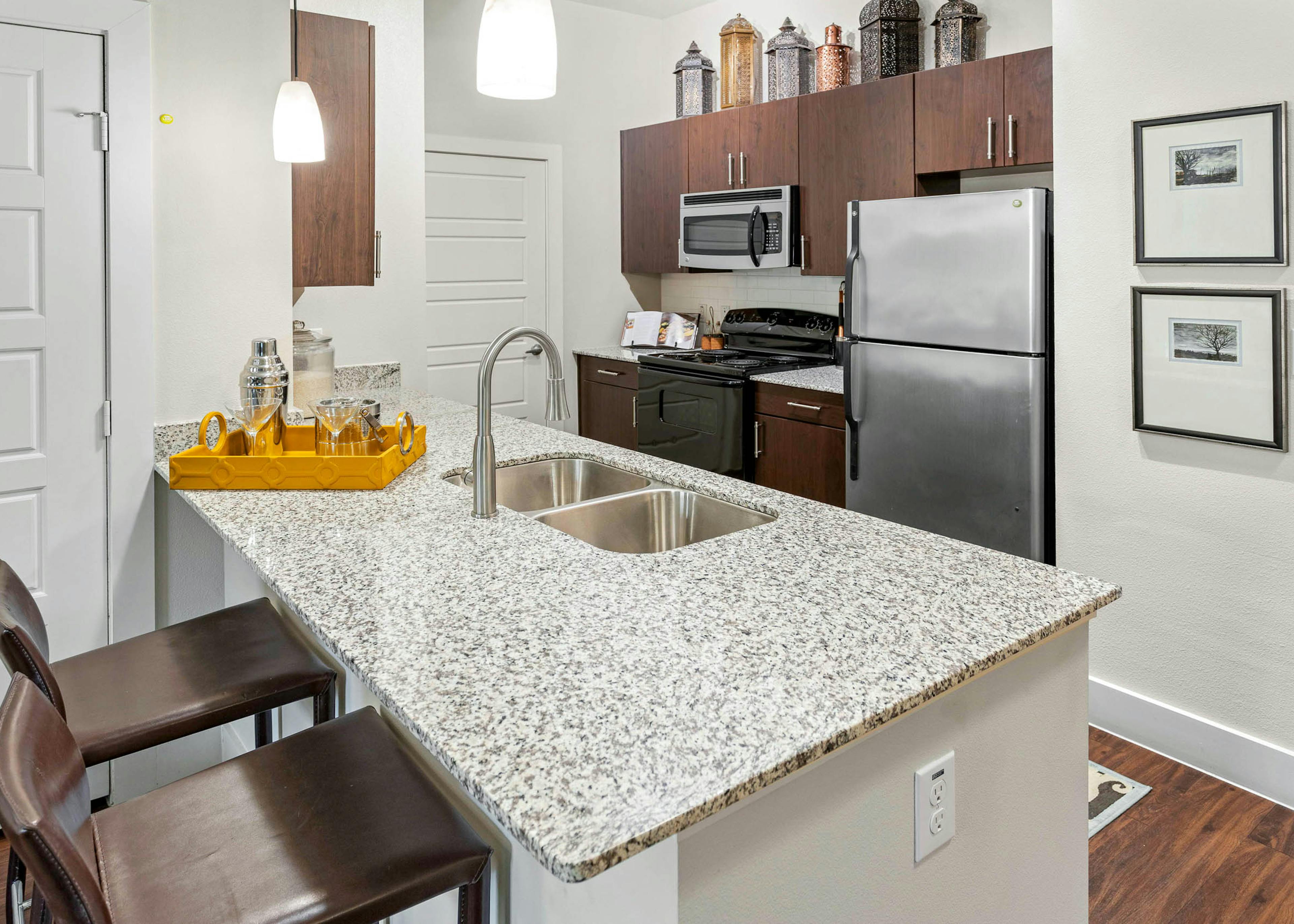 AMLI at Escena apartment kitchen with wooden cabinets and a yellow tray with drinking glasses on granite countertop 