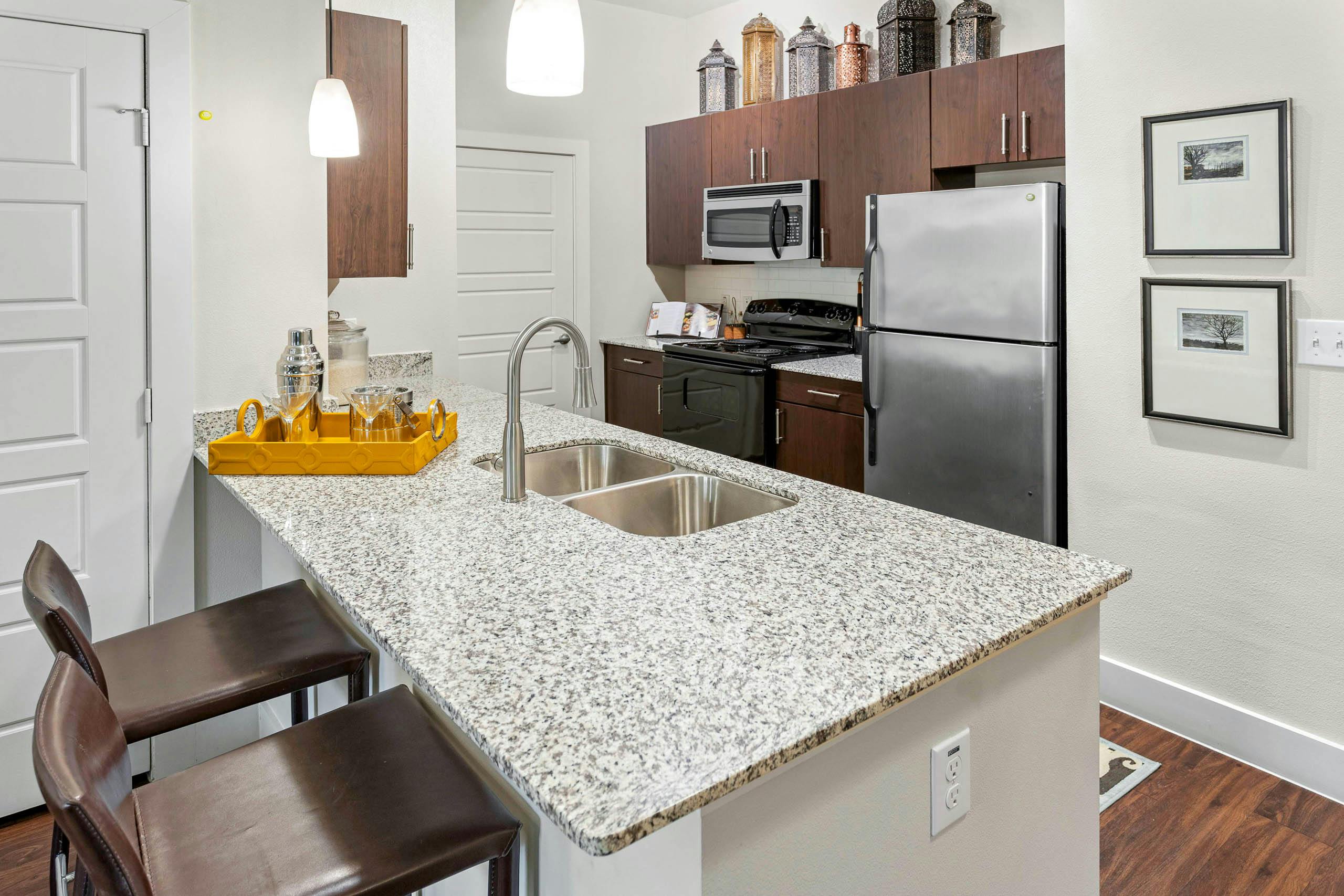 AMLI at Escena apartment kitchen with wooden cabinets and a yellow tray with drinking glasses on granite countertop