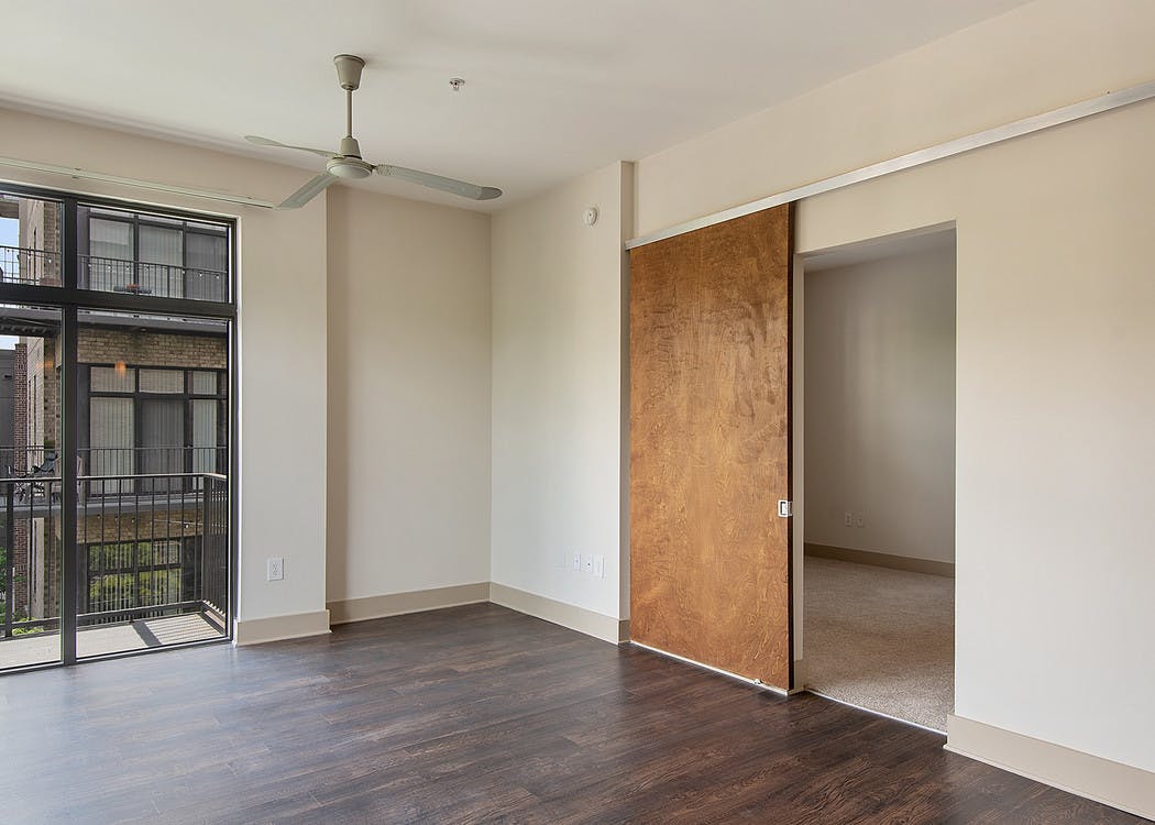 Interior of AMLI Old 4th Ward apartment living room with high ceilings, cream walls, dark hardwood and sliding wall panels