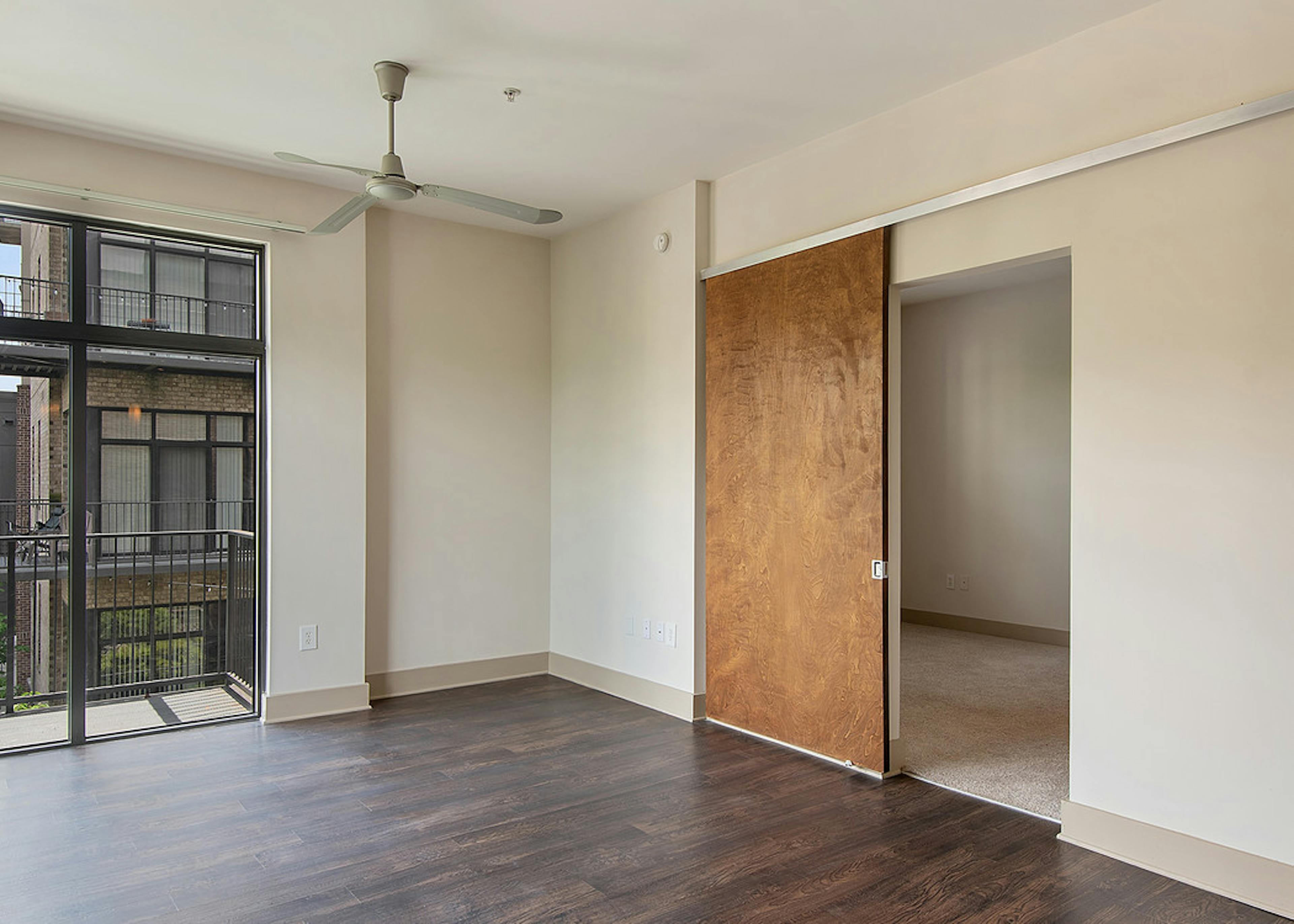 Interior of AMLI Old 4th Ward apartment living room with high ceilings, cream walls, dark hardwood and sliding wall panels
