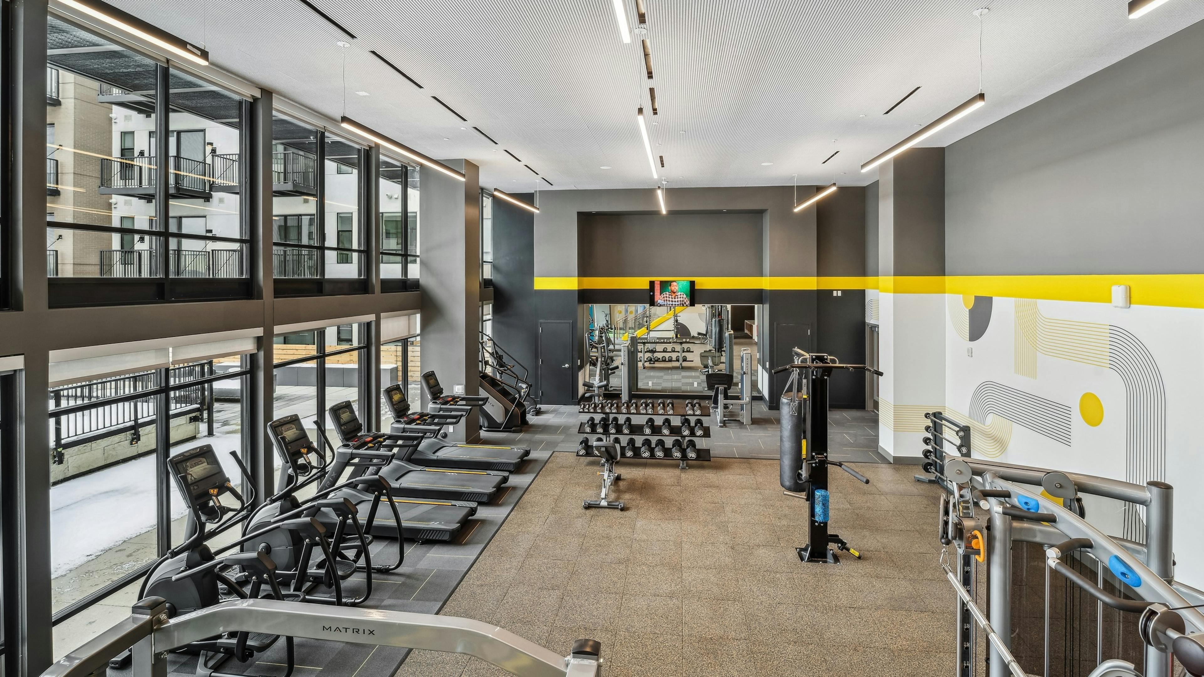 Interior view of a fitness center at AMLI Broadway Park with vaulted ceilings and several cardio machines as well as weights