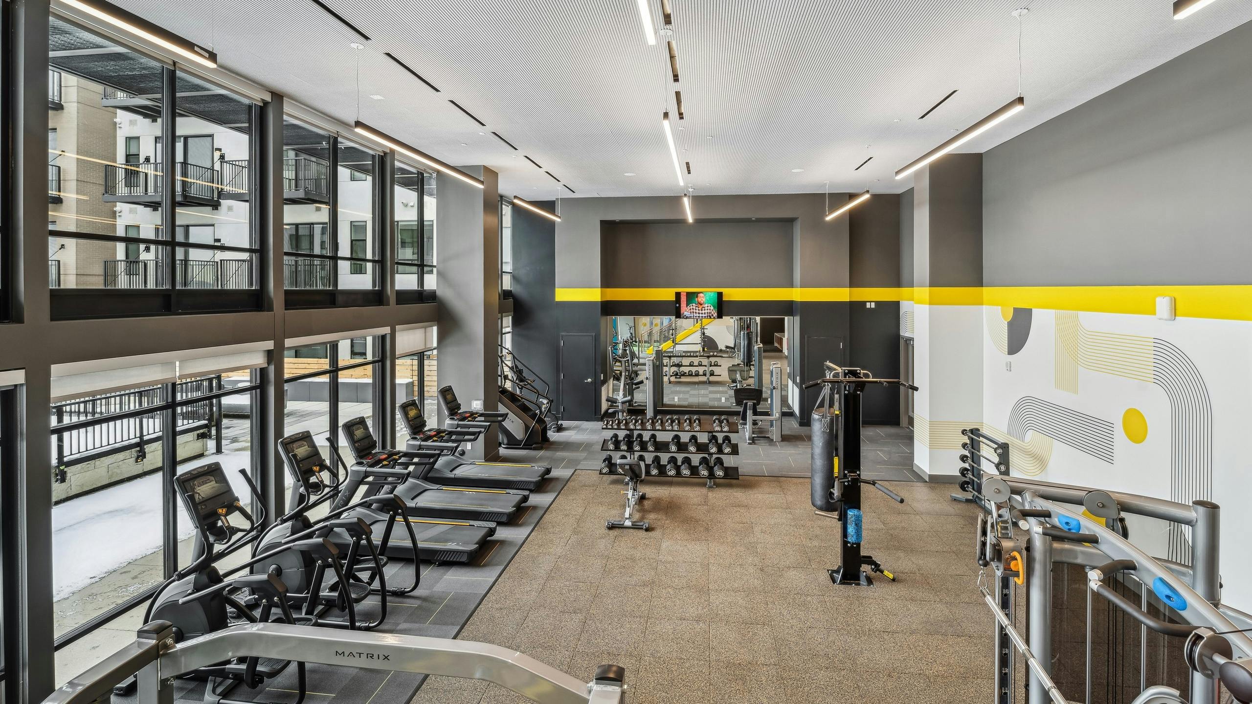 Interior view of a fitness center at AMLI Broadway Park with vaulted ceilings and several cardio machines as well as weights