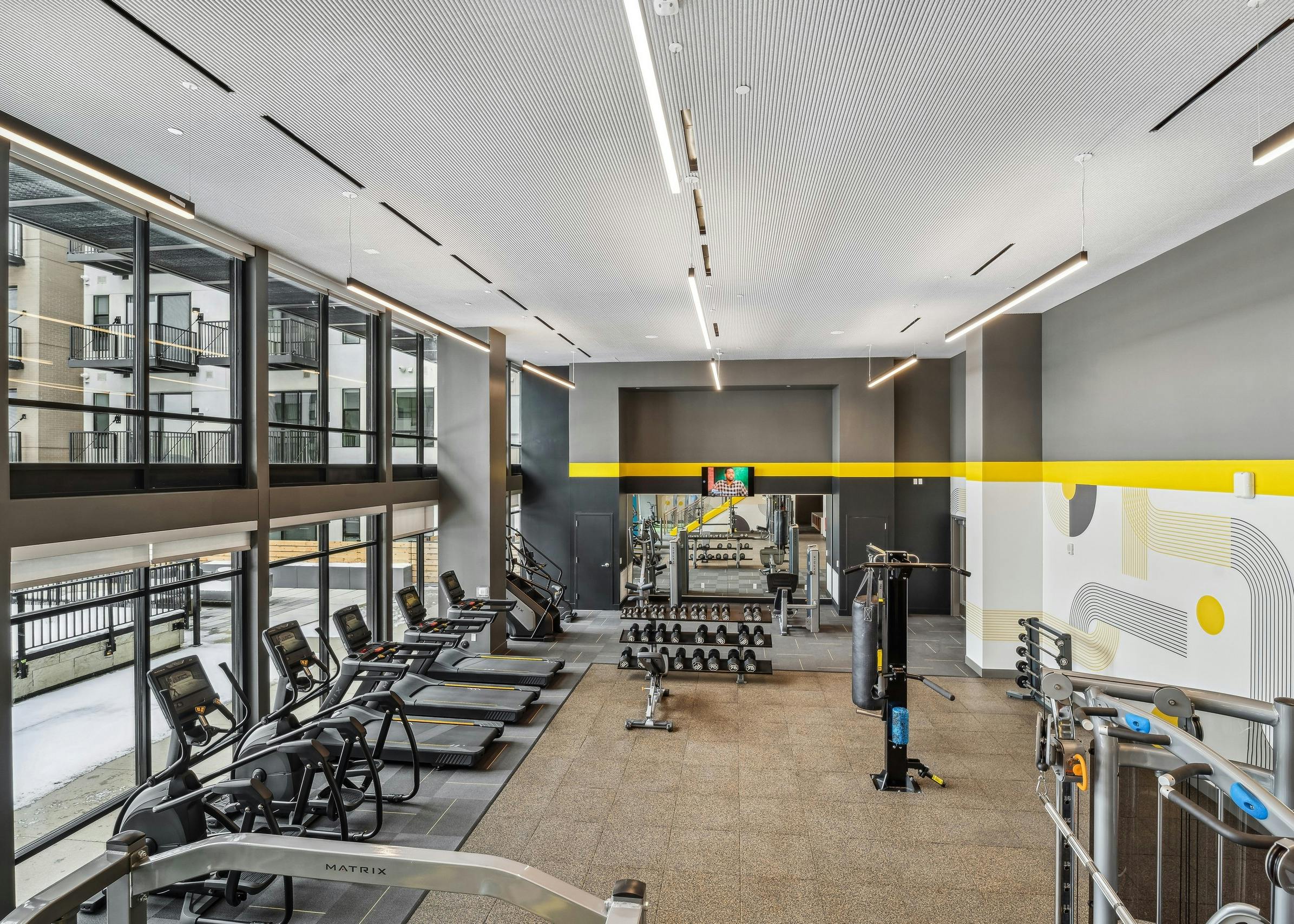 Interior view of a fitness center at AMLI Broadway Park with vaulted ceilings and several cardio machines as well as weights