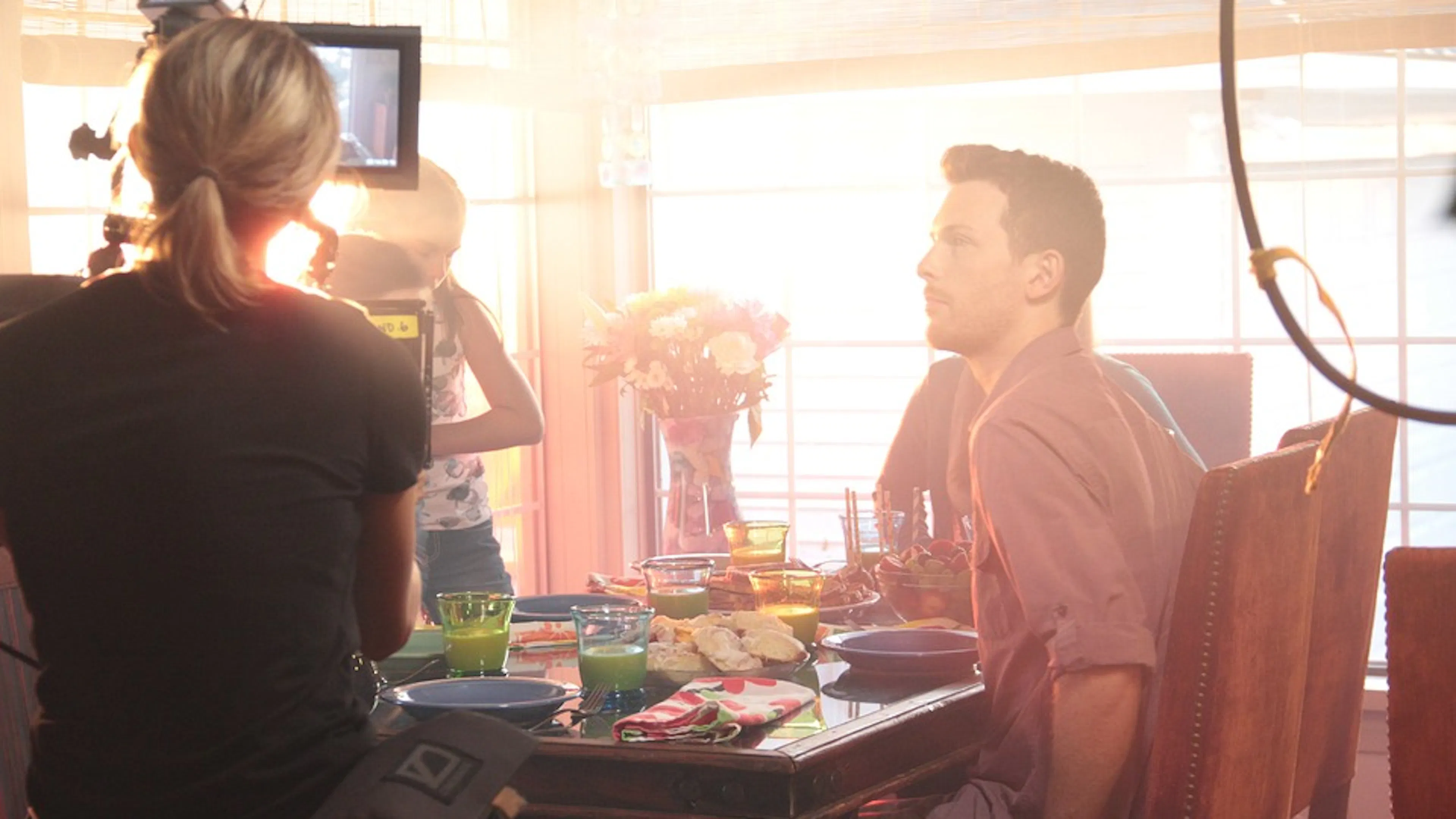 A woman filming a family at a dinner table through a cinematic camera on the set of a film