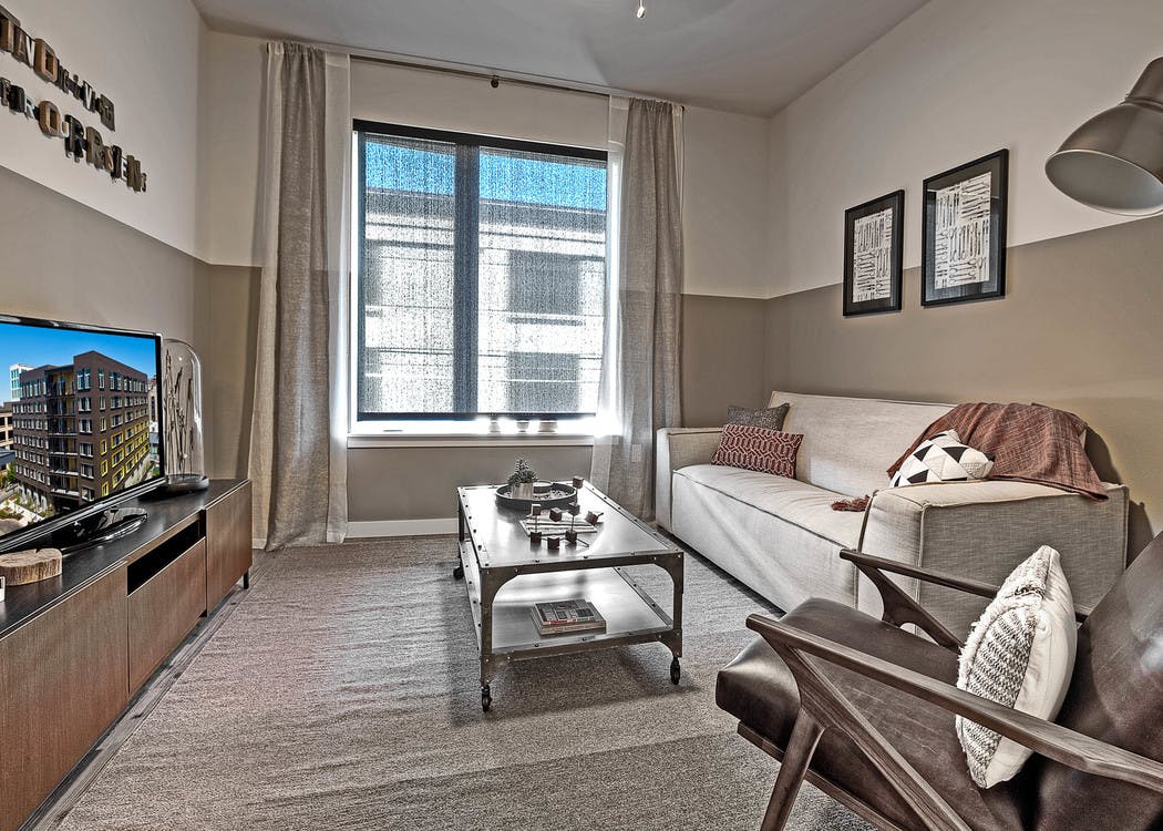 Living room with tan and white walls and couch and coffee table with tv and large window in an apartment at AMLI South Lake Union.