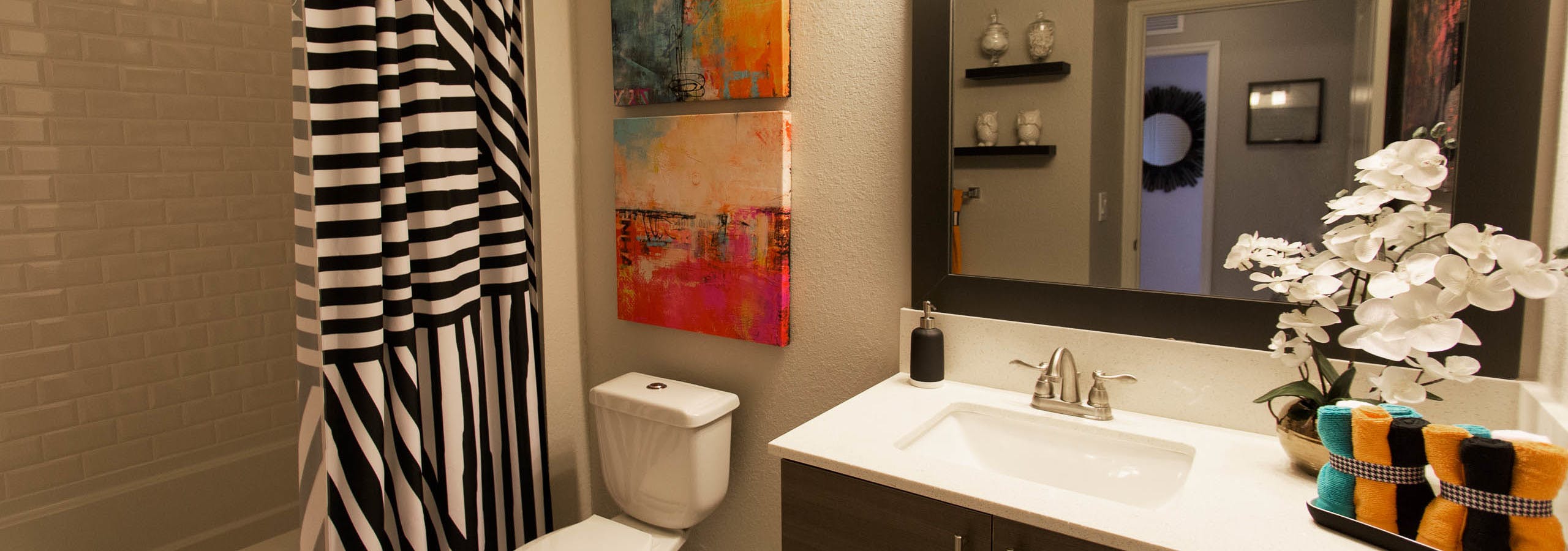 Interior view of bathroom at AMLI Dadeland apartments with single sink vanity, mirror and black and white shower curtain