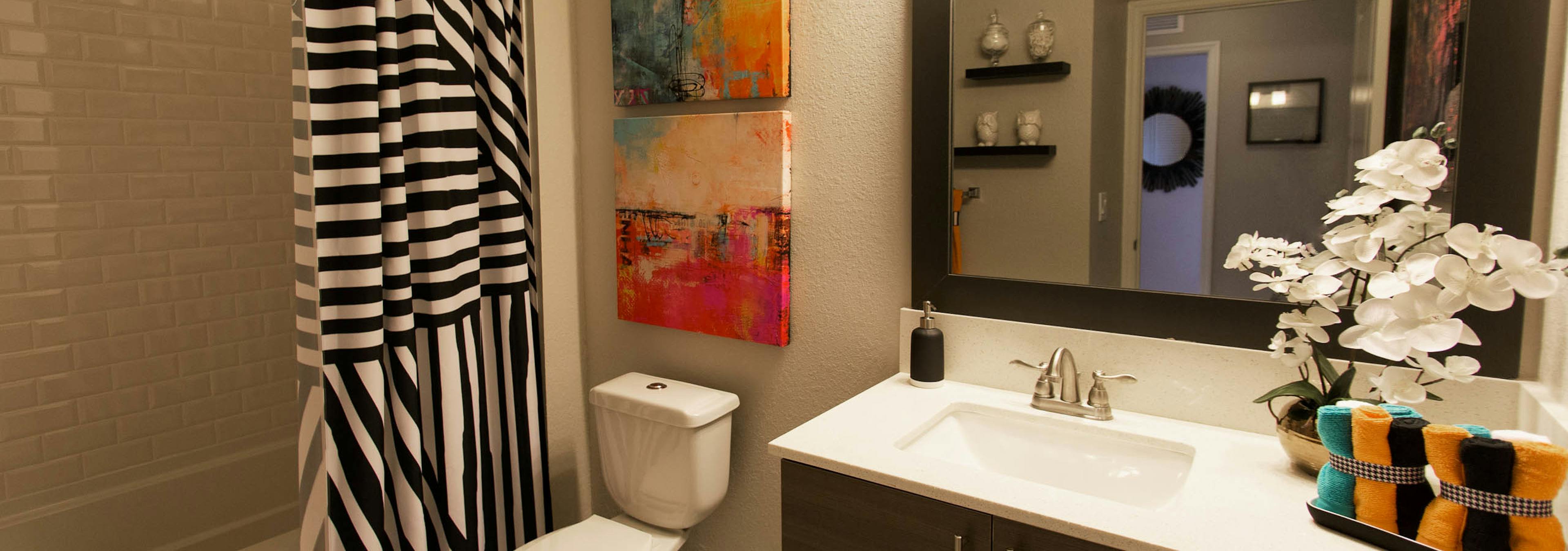 Interior view of bathroom at AMLI Dadeland apartments with single sink vanity, mirror and black and white shower curtain