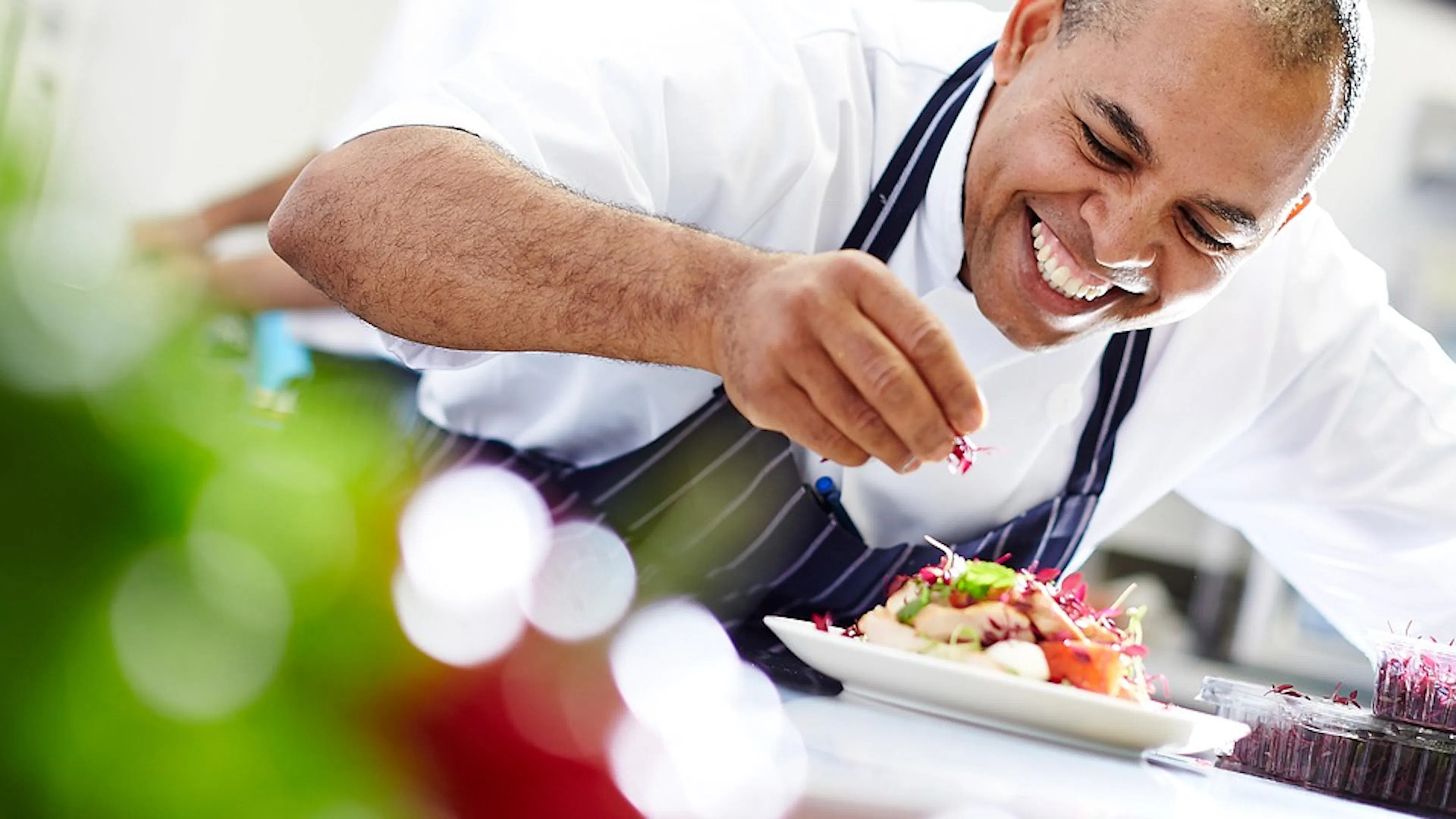 A chef garnishing a plate of salad on a bright white table