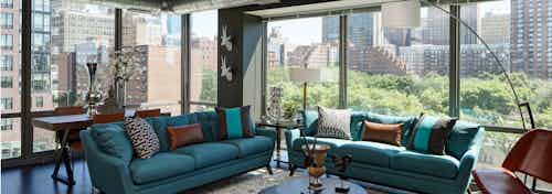 A luxurious AMLI 900 living room which features large glass windows overlooking surrounding city buildings and bright foliage