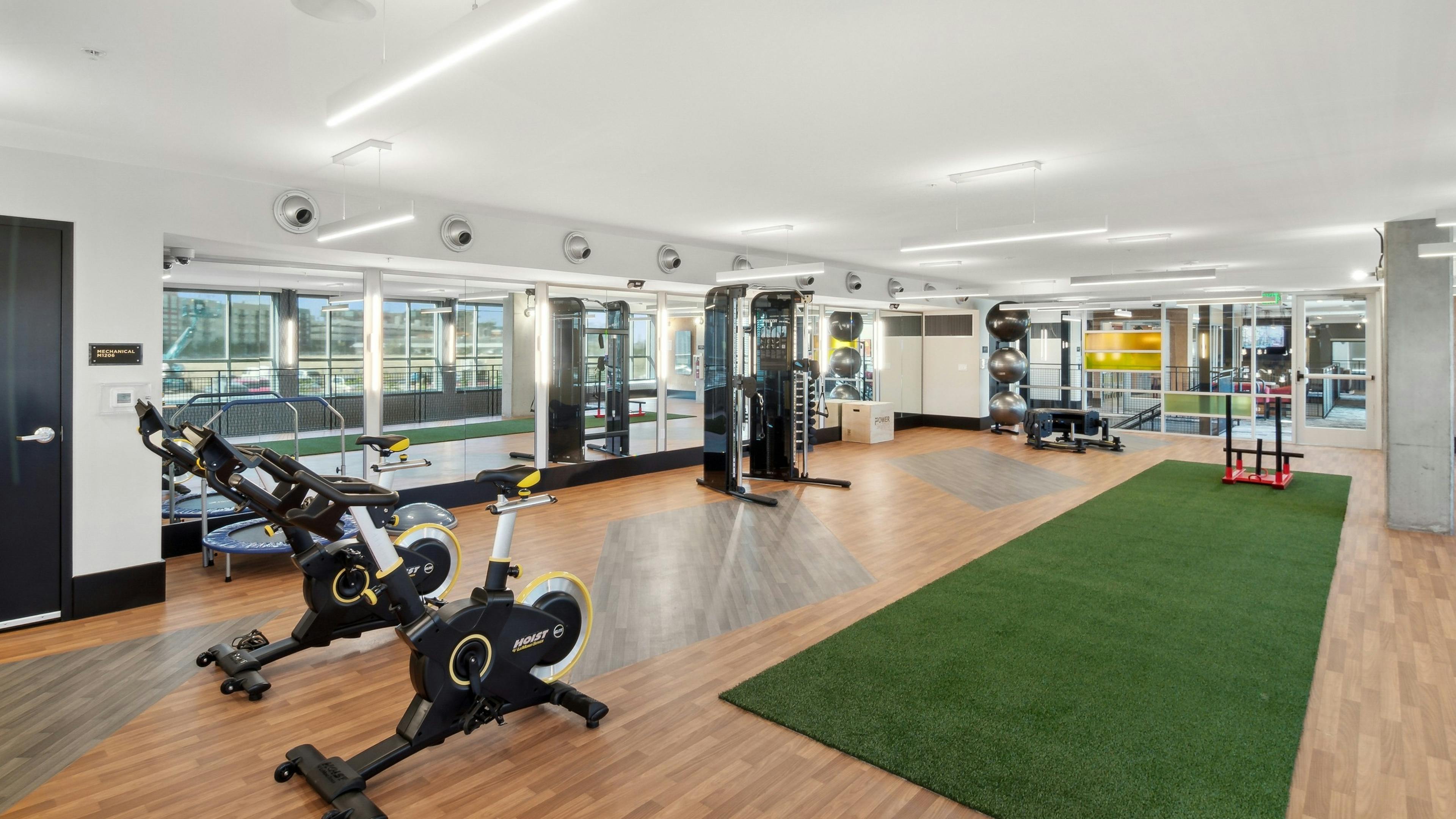 Yoga and spin room at AMLI RiNo apartments with spin bikes and weights with green turf workout area and mirrored wall
