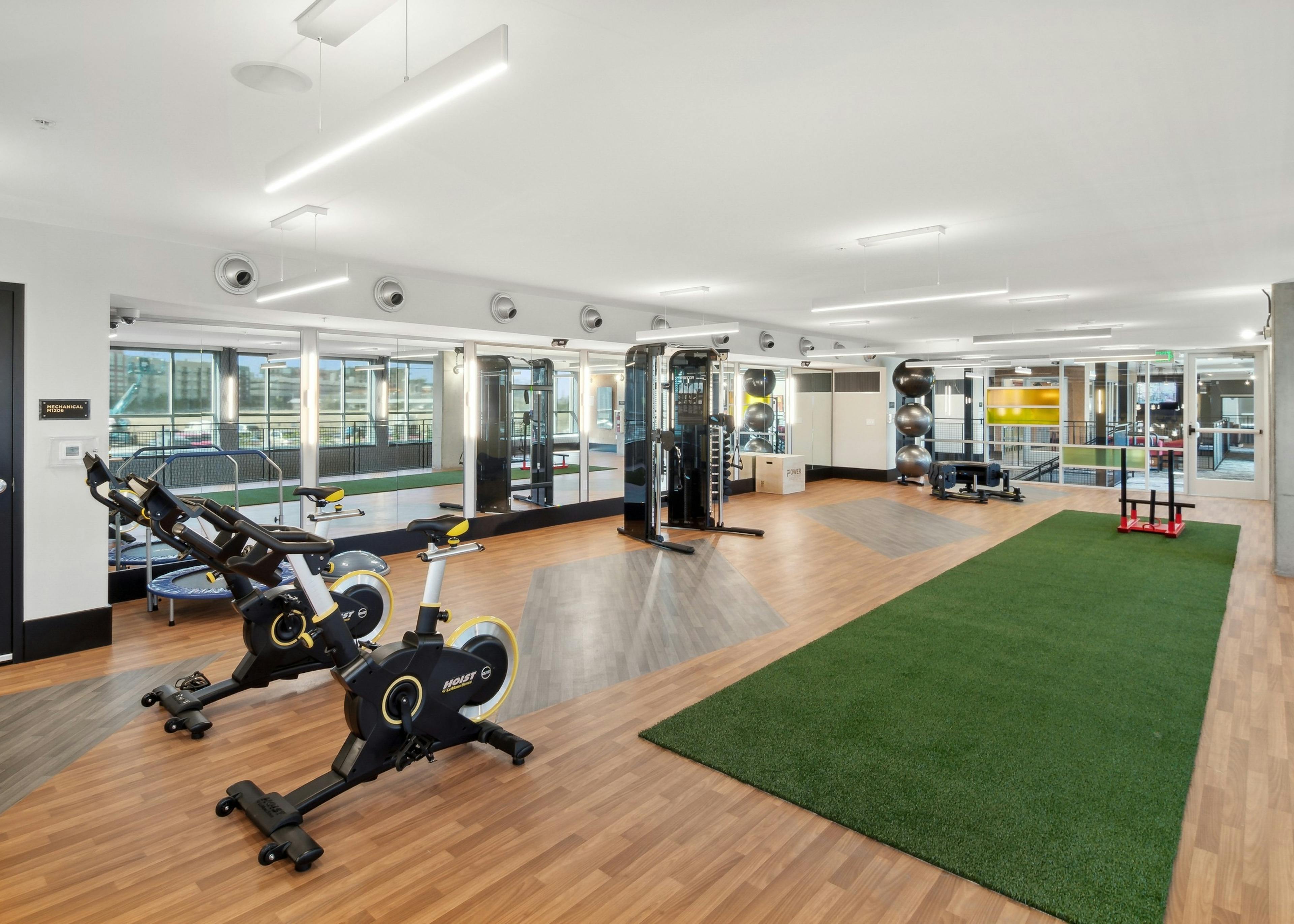 Yoga and spin room at AMLI RiNo apartments with spin bikes and weights with green turf workout area and mirrored wall
