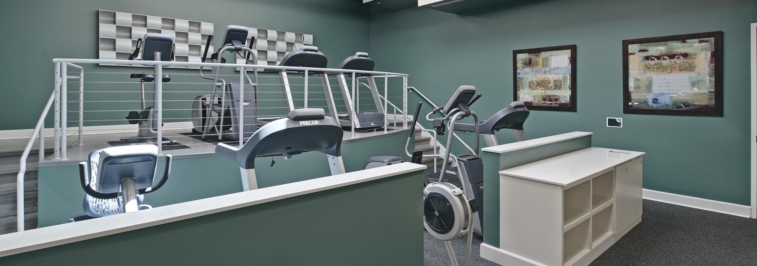 Interior view of AMLI Evanston fitness center with teal walls and grey flooring featuring treadmills and elliptical machines