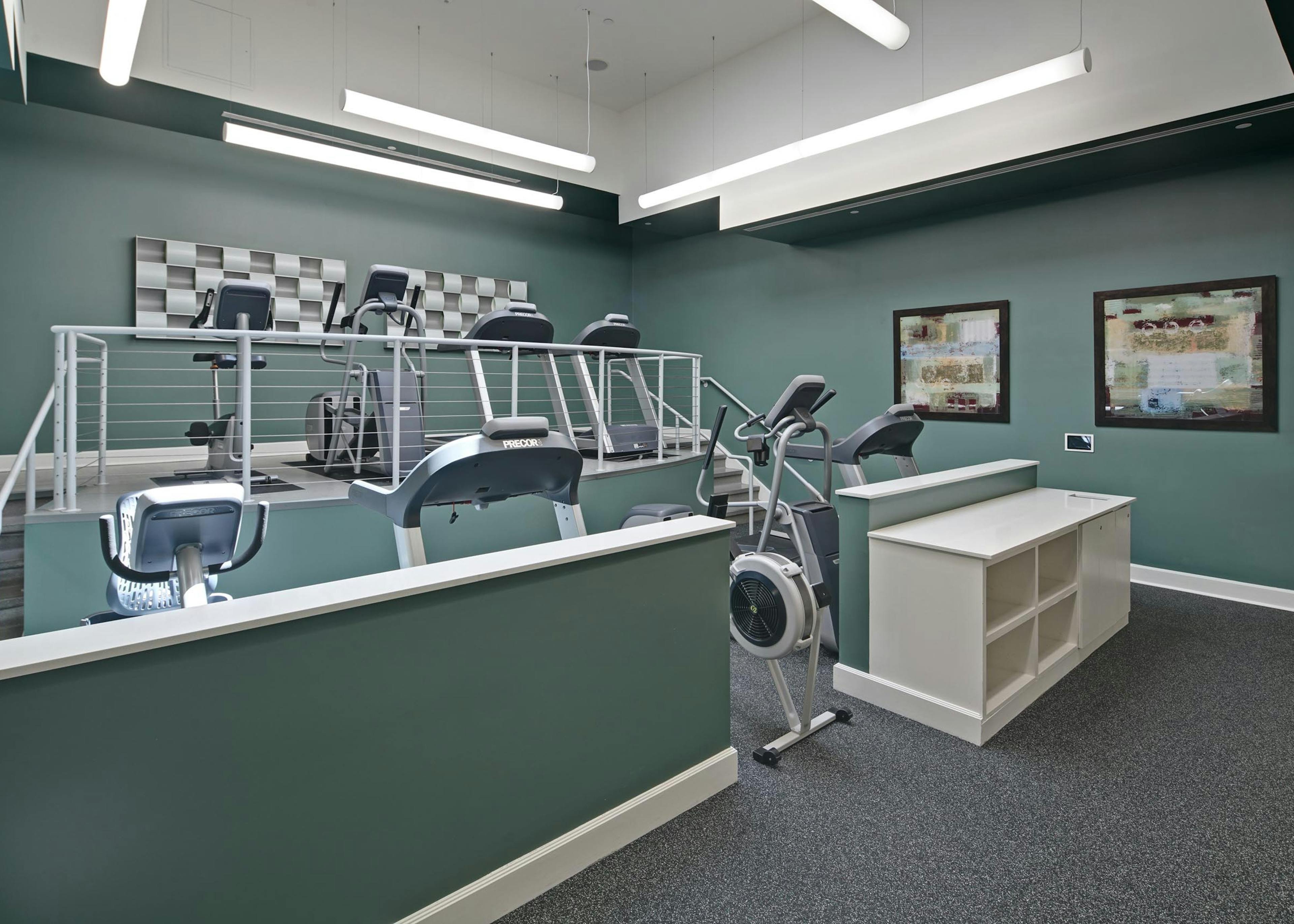 Interior view of AMLI Evanston fitness center with teal walls and grey flooring featuring treadmills and elliptical machines