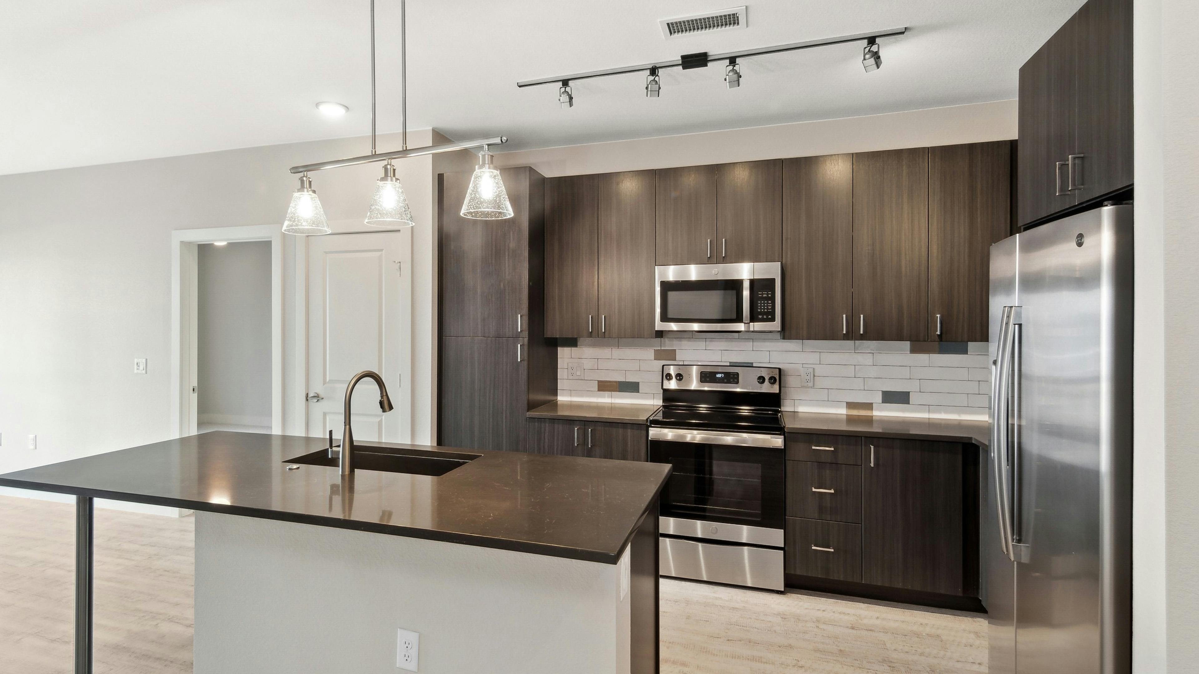 Island kitchen with dark countertops and cabinets with white tile backsplash and stainless appliances at AMLI RiNo