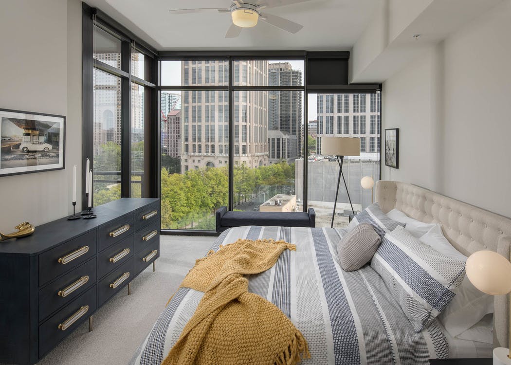 AMLI Arts Center bedroom with neutral walls and white patterned bedding with bright city view out of floor to ceiling windows