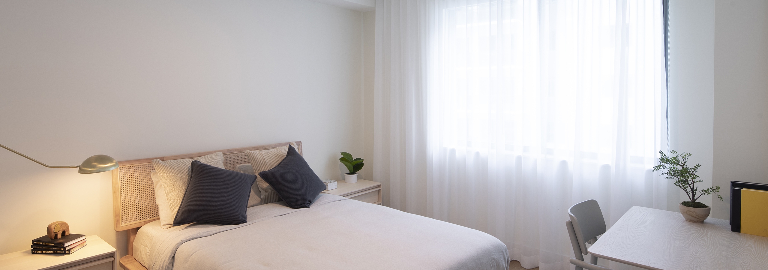 Interior of AMLI Midtown Miami apartment bedroom with bed centered on wall and desk with chair near large curtained window