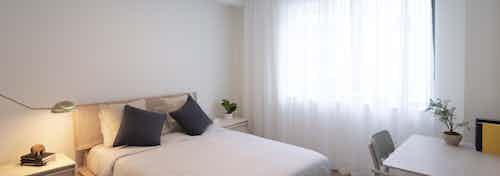 Interior of AMLI Midtown Miami apartment bedroom with bed centered on wall and desk with chair near large curtained window