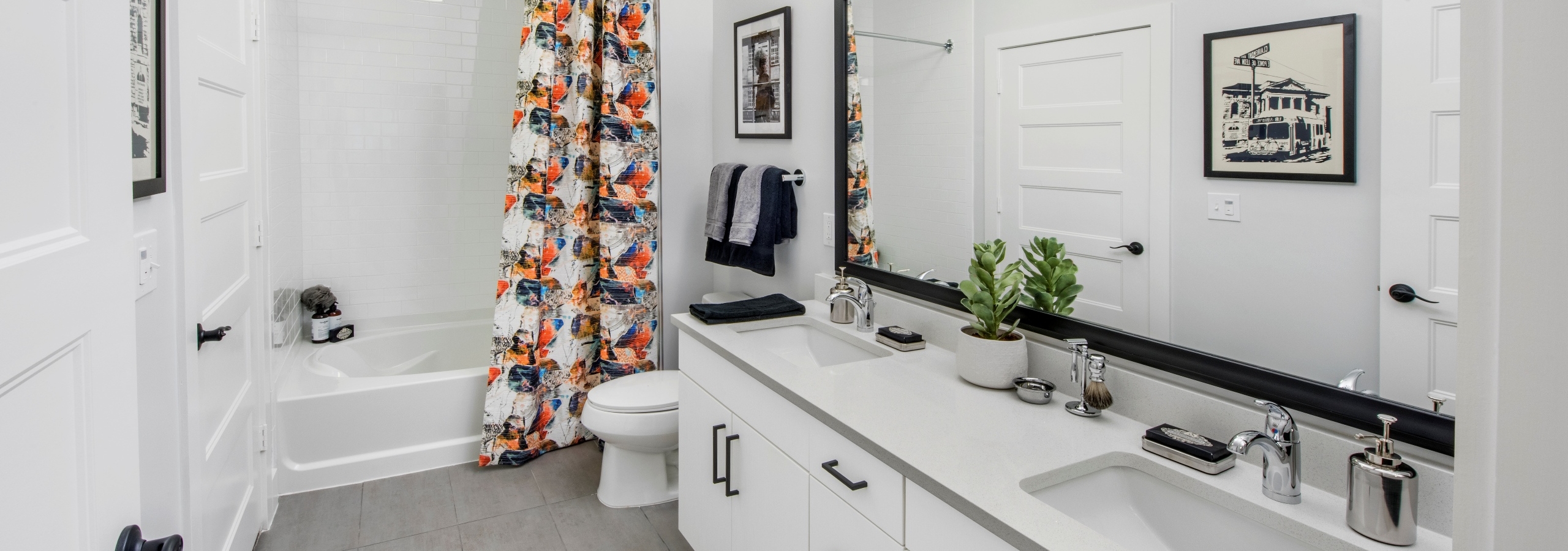 AMLI Decatur apartment bathroom with a white double vanity with a framed mirror and soaking tub with patterned curtain