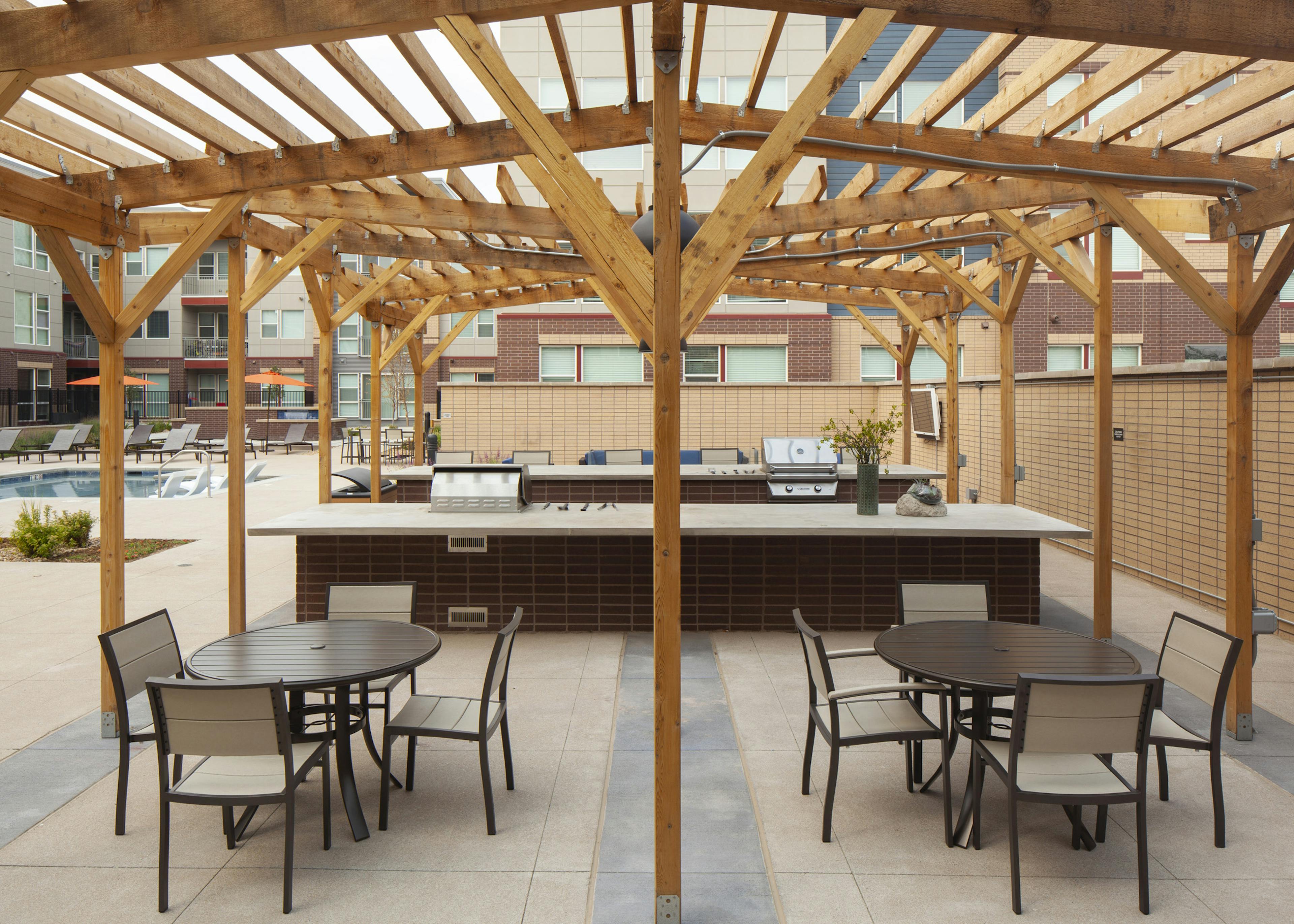Exterior view of a grilling area at AMLI Littleton Village pool with 2 grills and 2 tables with chairs and a large wood canopy