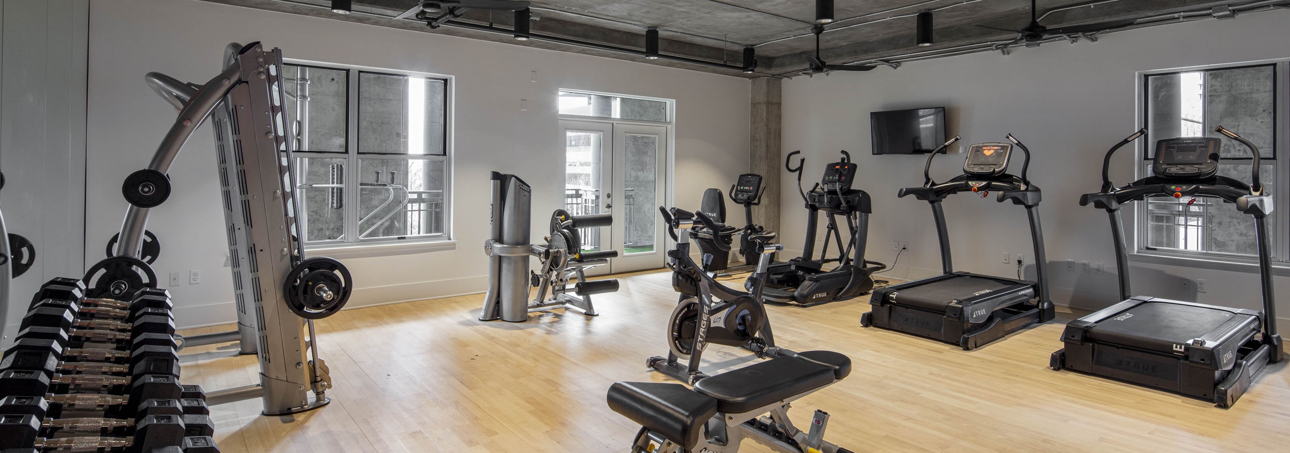 AMLI Downtown fitness center with free weights rack and cardio machines on a light wooden floor with concrete ceiling above
