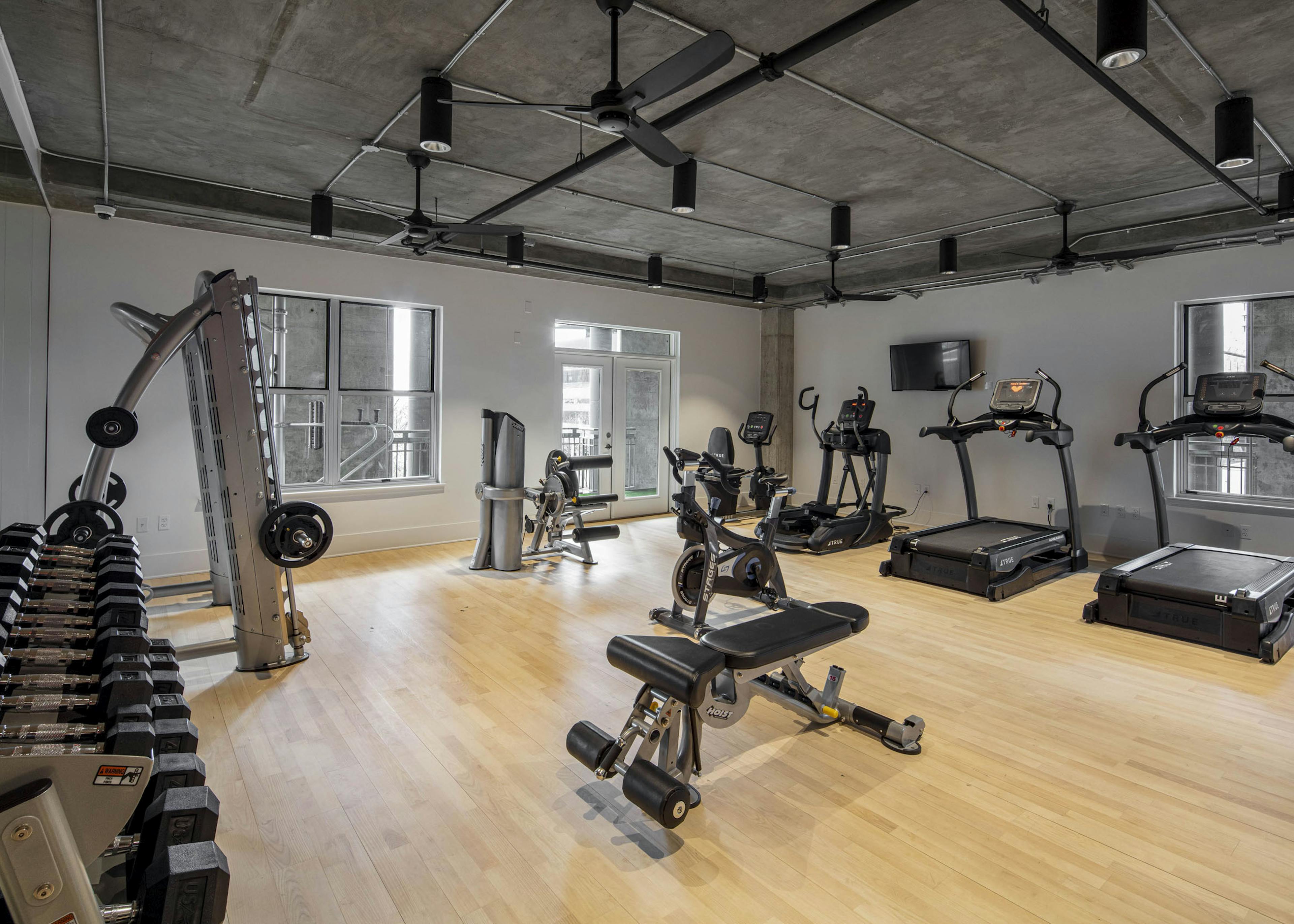 AMLI Downtown fitness center with free weights rack and cardio machines on a light wooden floor with concrete ceiling above