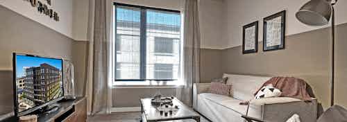 Living room with tan and white walls and couch and coffee table with tv and large window in an apartment at AMLI South Lake Union.