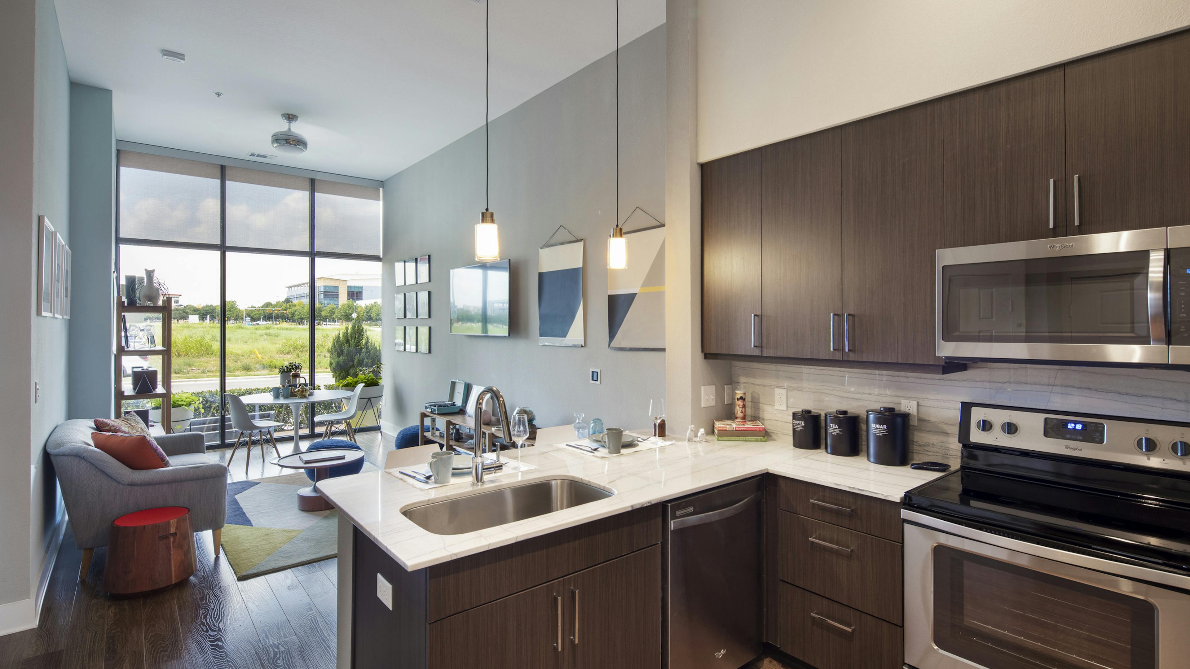 AMLI on Aldrich apartment kitchen with brown cabinets looking into furnished living room and wall of windows and view of field