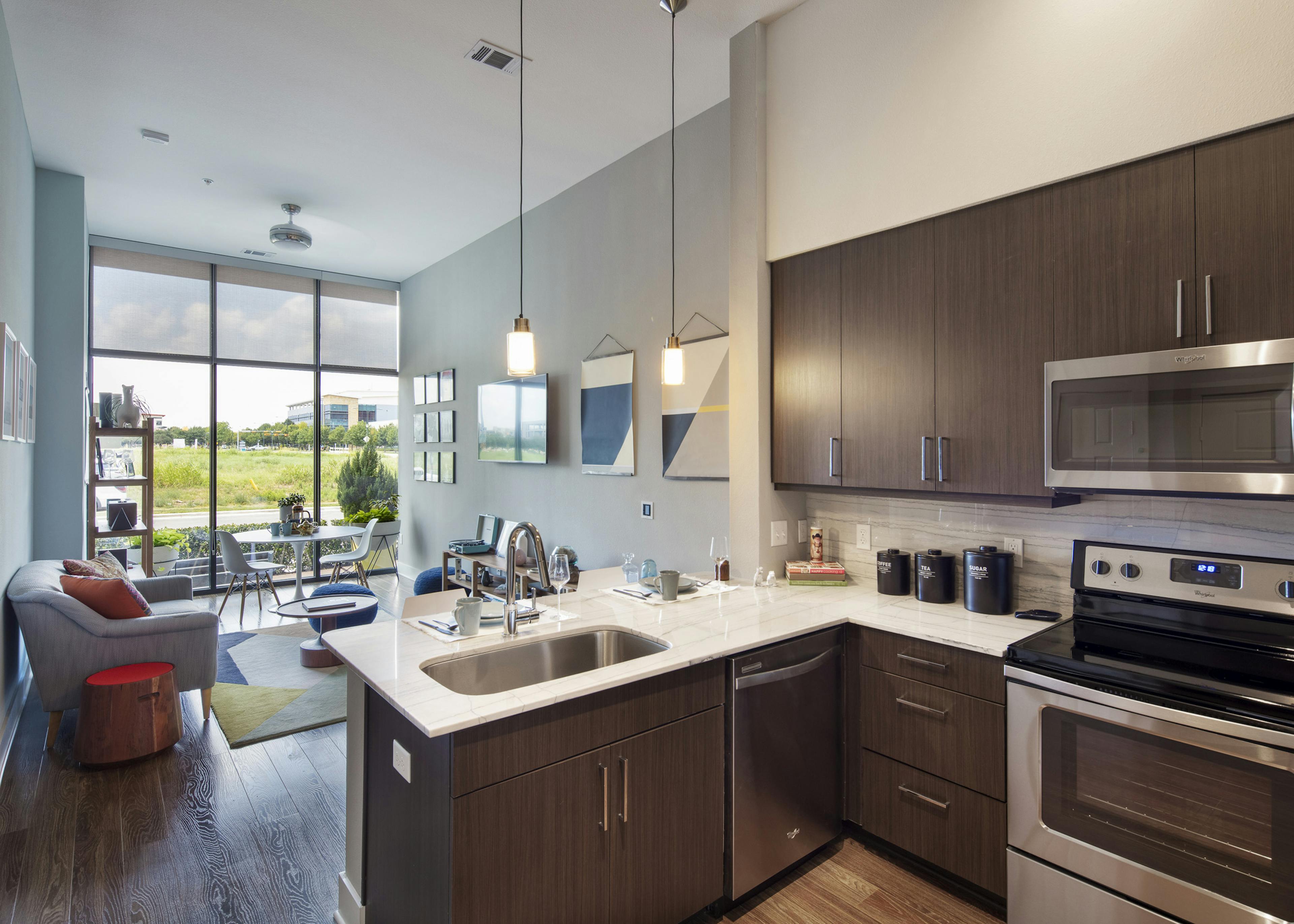 AMLI on Aldrich apartment kitchen with brown cabinets looking into furnished living room and wall of windows and view of field