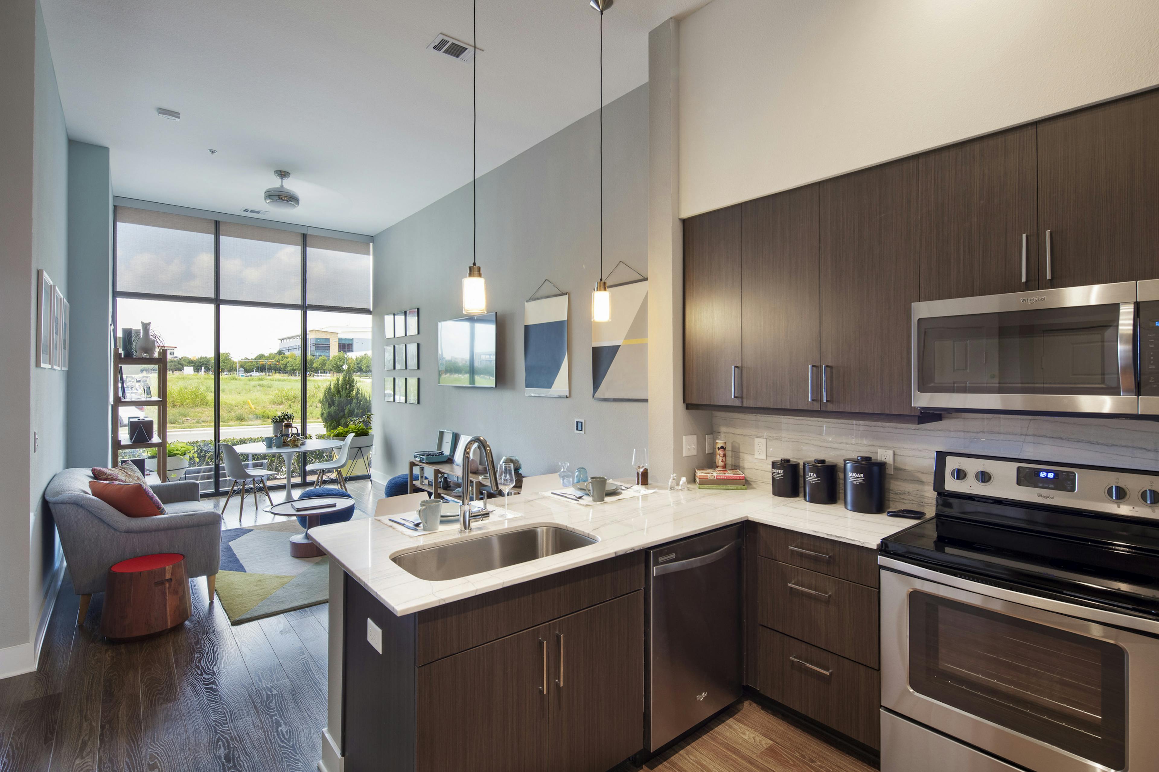 AMLI on Aldrich apartment kitchen with brown cabinets looking into furnished living room and wall of windows and view of field