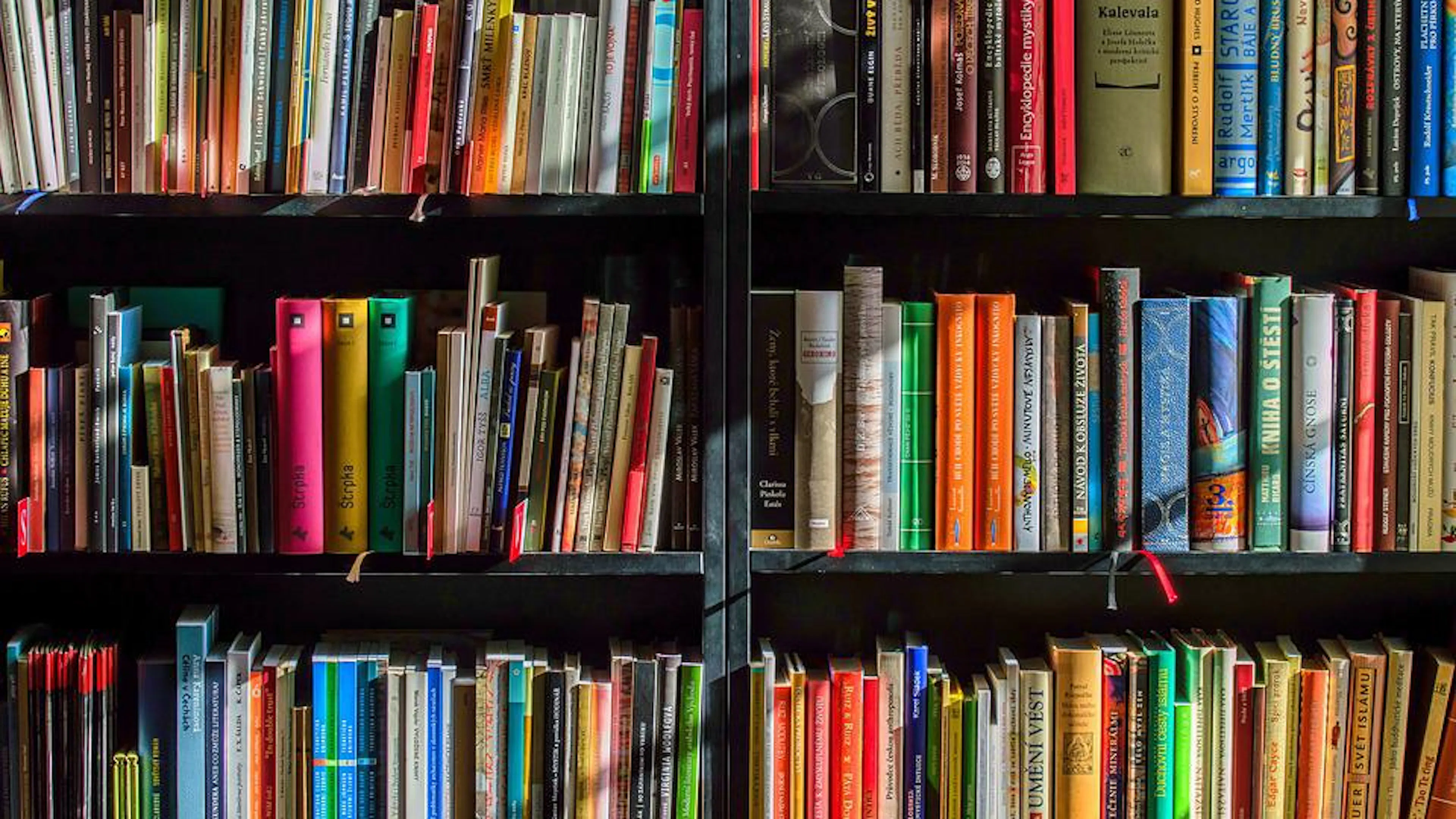 A close up of a bookshelf with colorful books arranged neatly on the dark wooden shelves